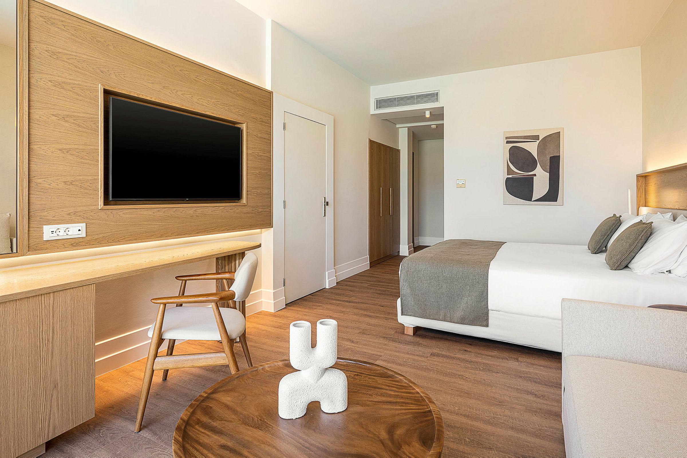 Et moderne hotelværelse med en dobbeltseng, et skrivebord med stol og et TV på væggen. Et lille bord står i forgrunden. (AI-genereret tekst)