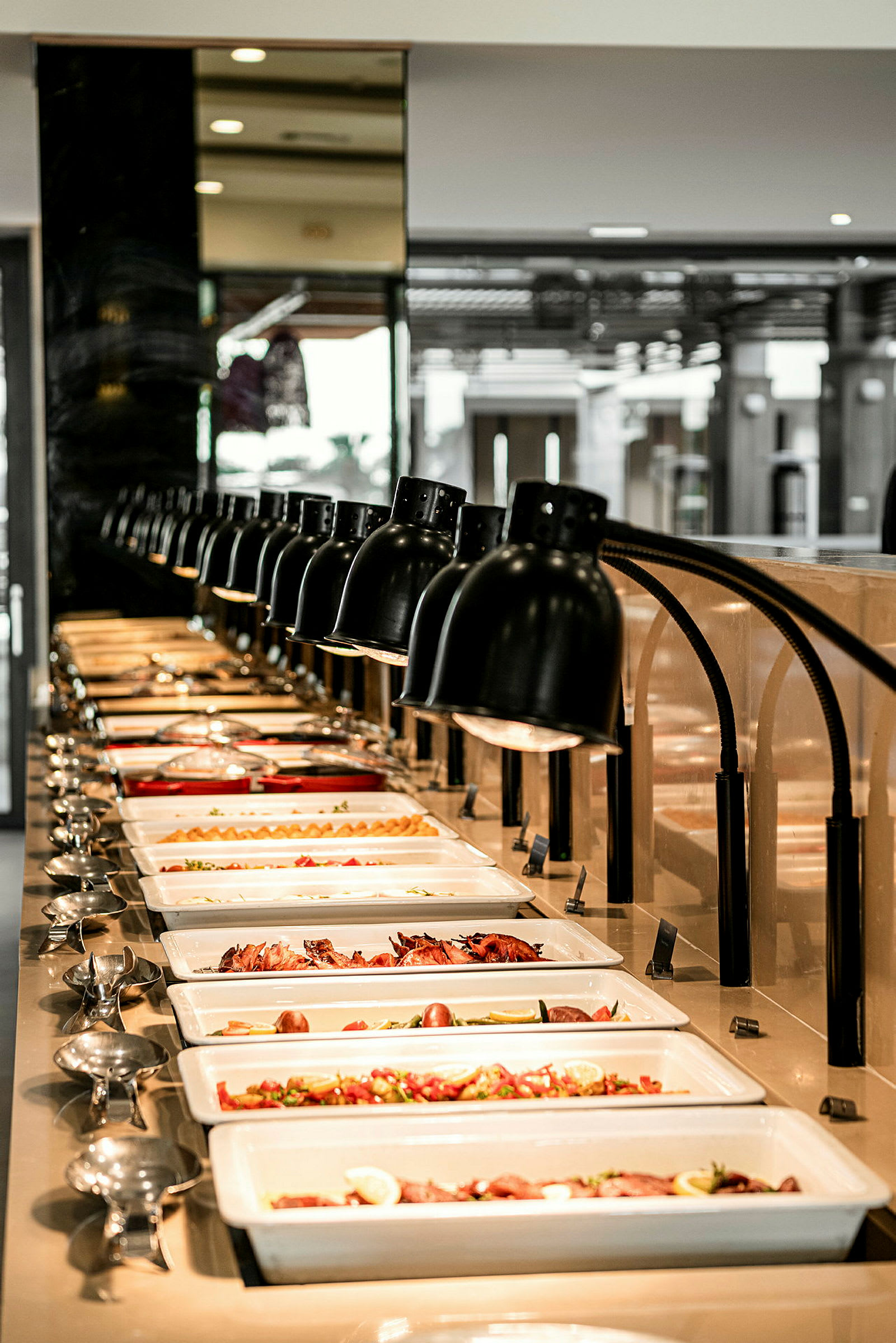 En buffet med forskellige retter præsenteret i rektangulære hvide tallerkener under rækker af lamper. (AI-genereret tekst)