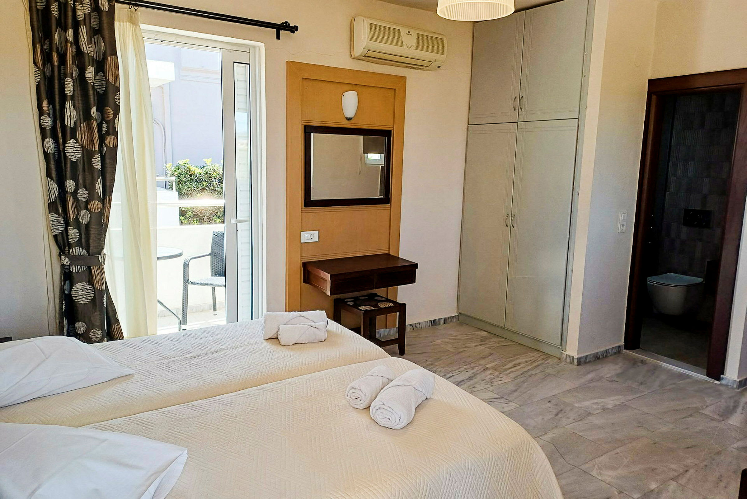 Hotelværelse med to enkeltsenge, et skrivebord og udsigt til en balkon med siddeplads. (AI-genereret tekst)