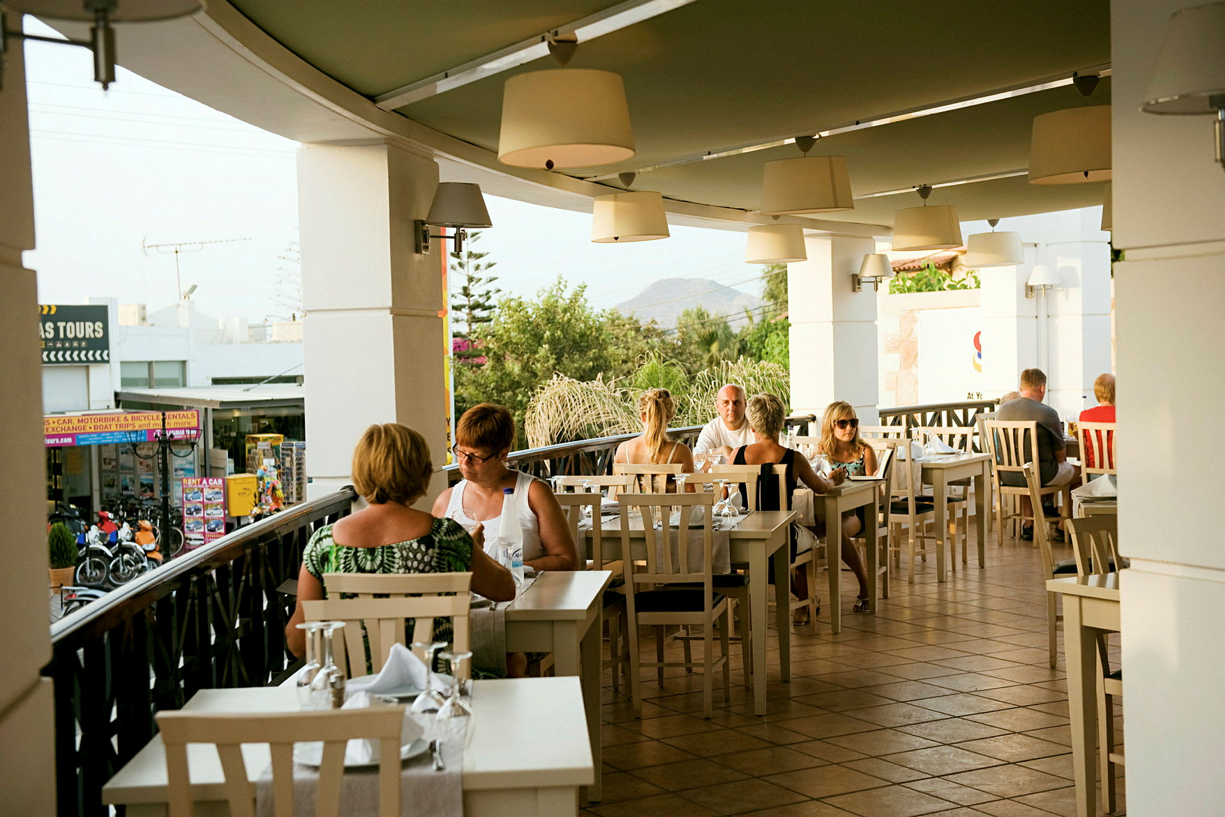 En udendørs restaurant med folk, der sidder ved borde. (AI-genereret tekst)