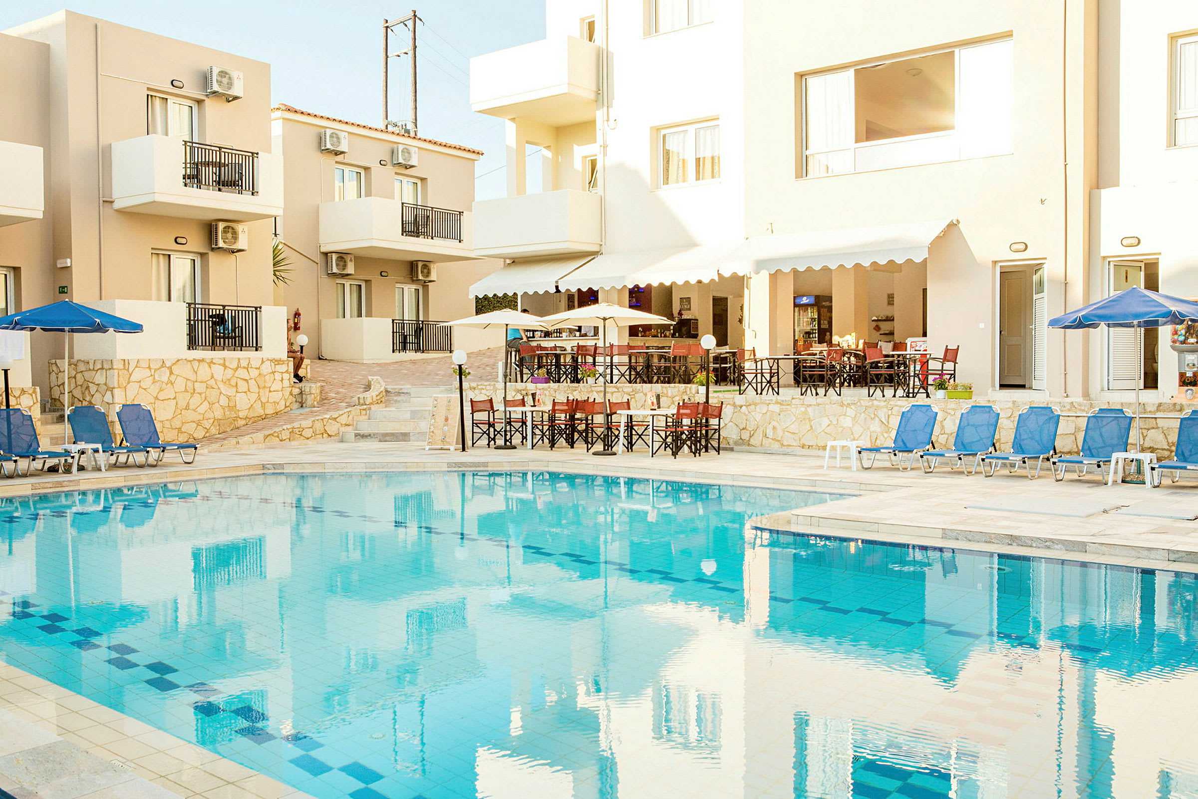 Billede af en hotelbygning med altaner og en pool med solsenge. (AI-genereret tekst)