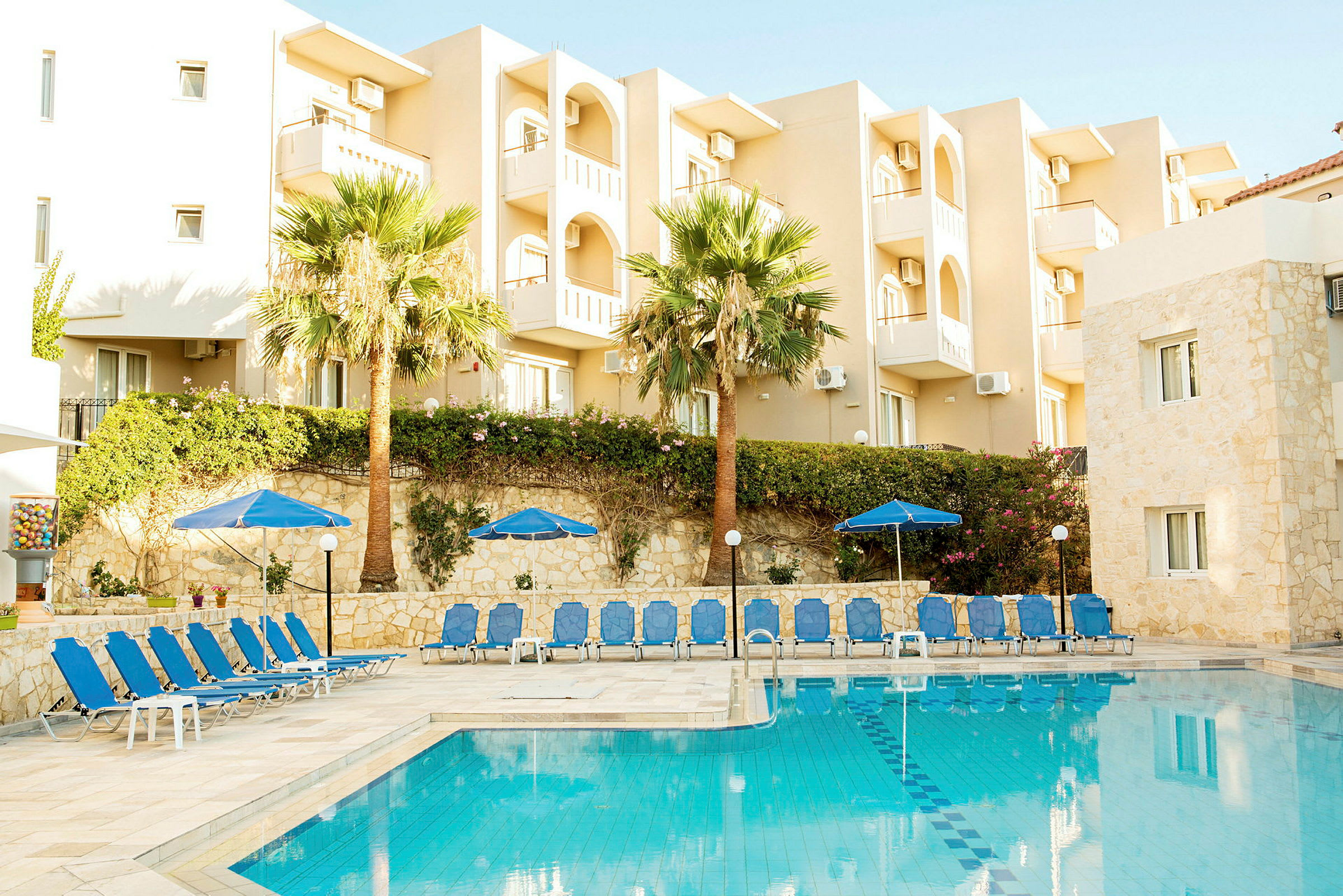 Hotelbygning med altaner ved siden af en pool, liggestole og parasoller. (AI-genereret tekst)