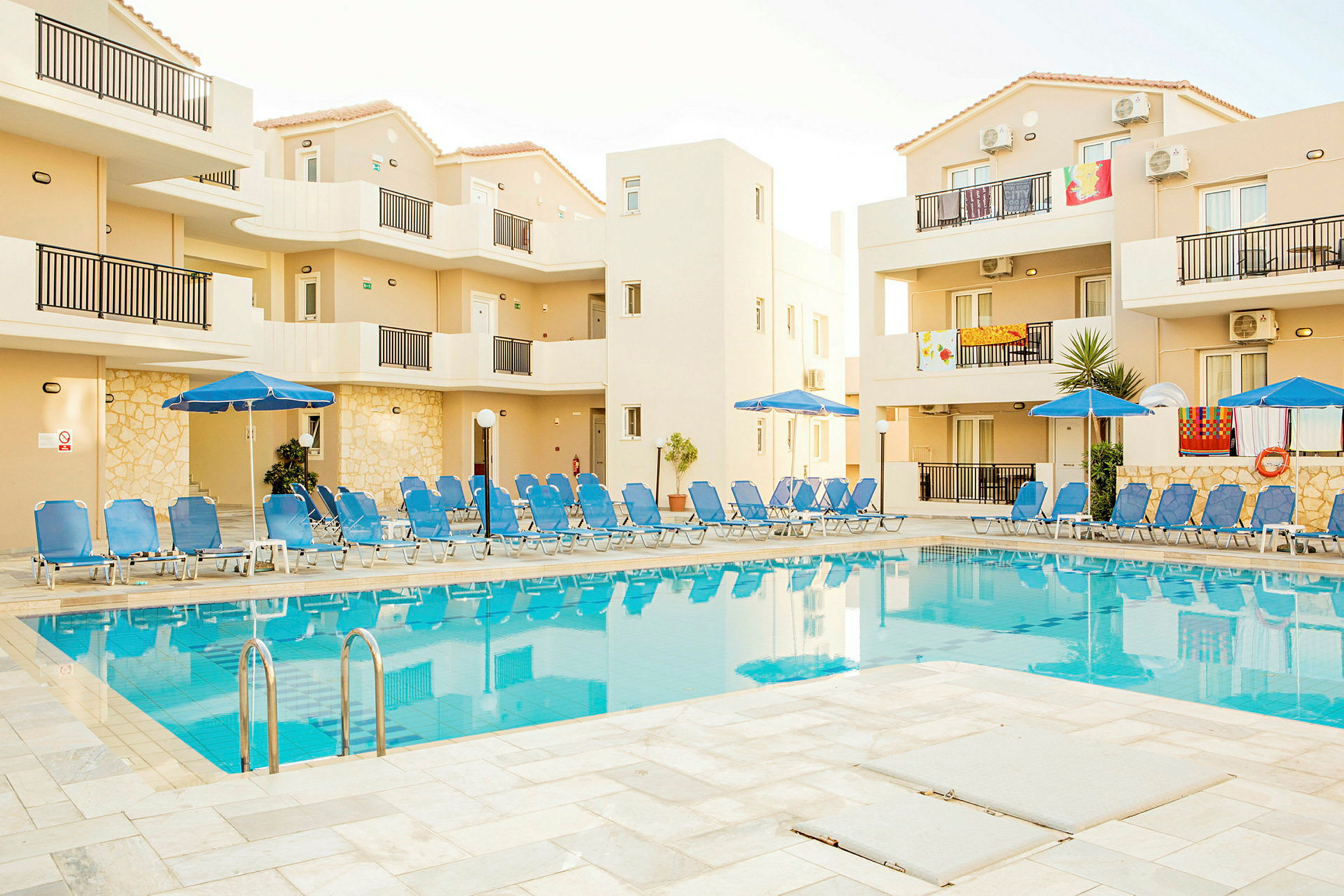 Billede af hotelbygning med en pool omgivet af solsenge. (AI-genereret tekst)