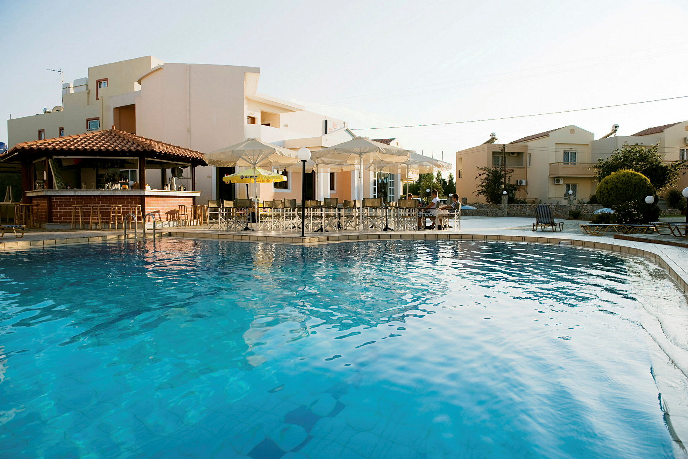 En swimmingpool foran bygninger med bar og parasoller. (AI-genereret tekst)