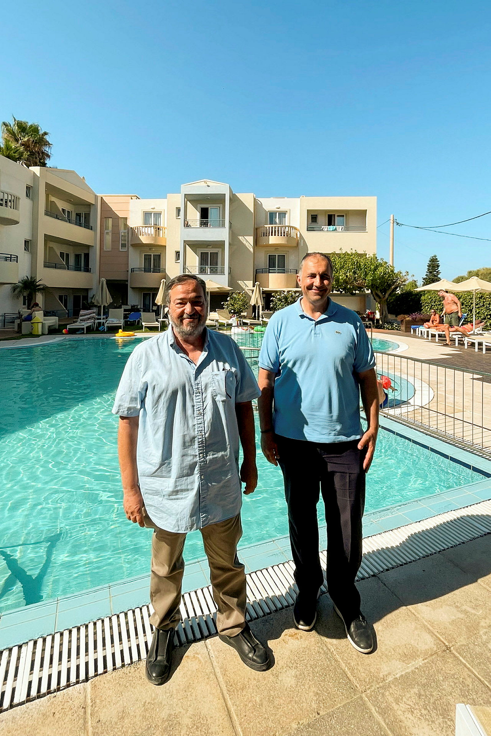 Personer står ved poolen foran et hotel. (AI-genereret tekst)