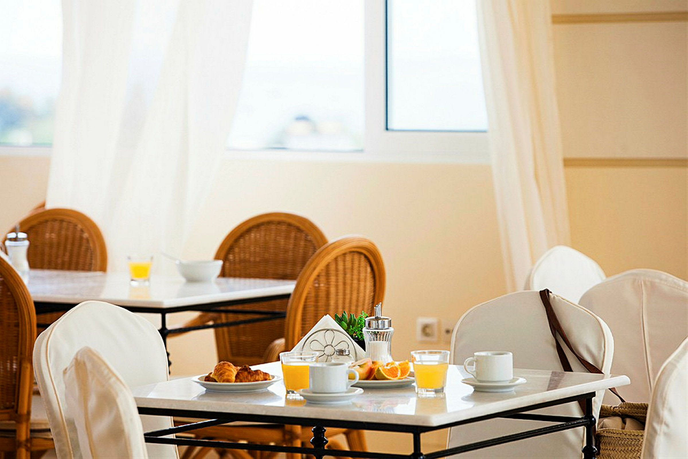 Et morgenmadssted med dækkede borde, hvide duge og morgenmadsartikler som juice, kaffe og brød. (AI-genereret tekst)