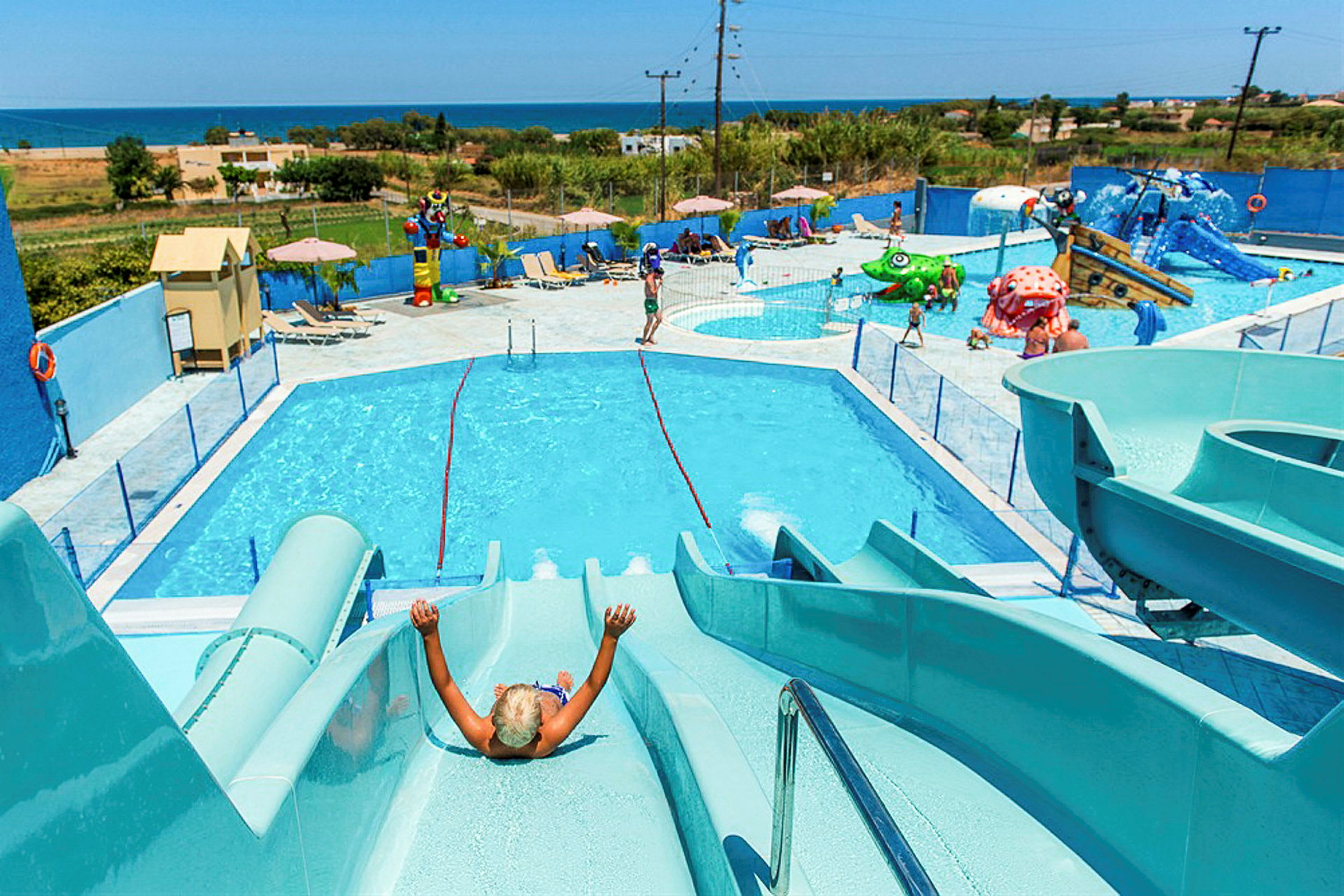 En vandpark med pools, vandrutsjebaner og legeområder, med udsigt over landskabet og havet. (AI-genereret tekst)