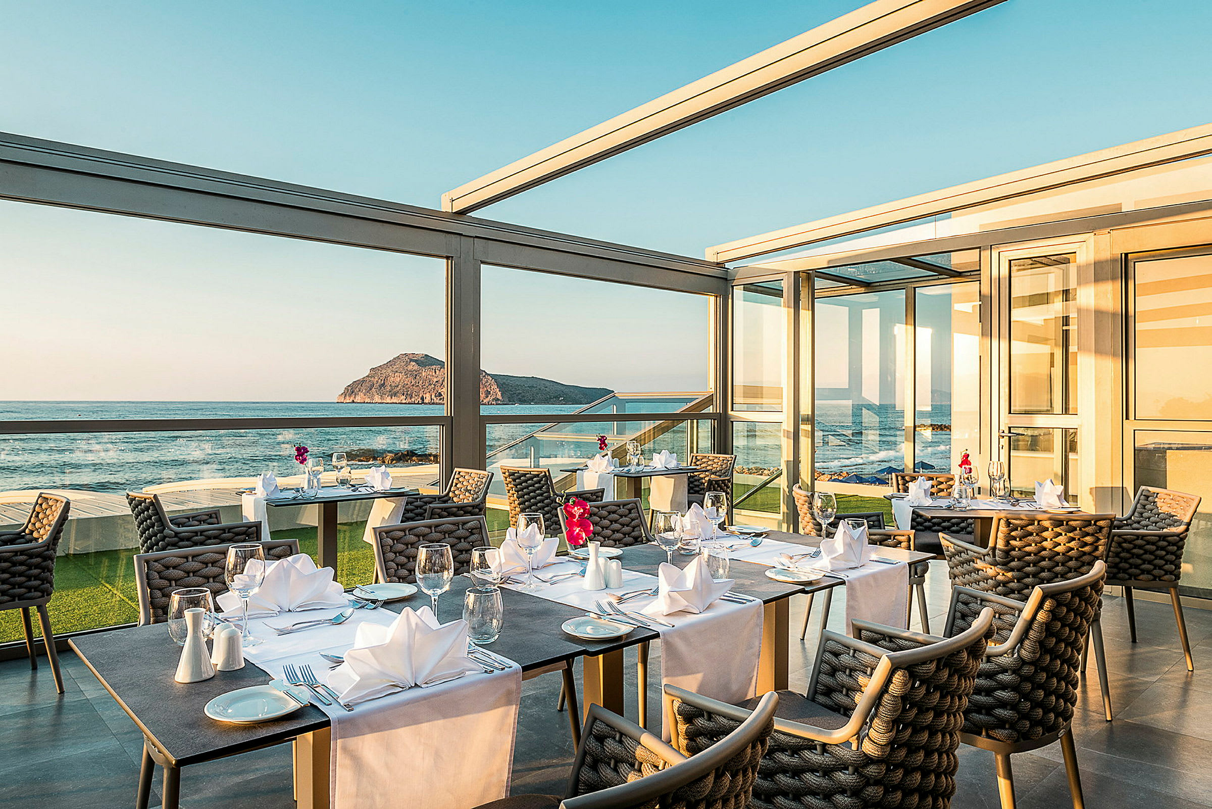 Restaurant med borde dækket op og stor vinduesudsigt mod hav og landskab. (AI-genereret tekst)