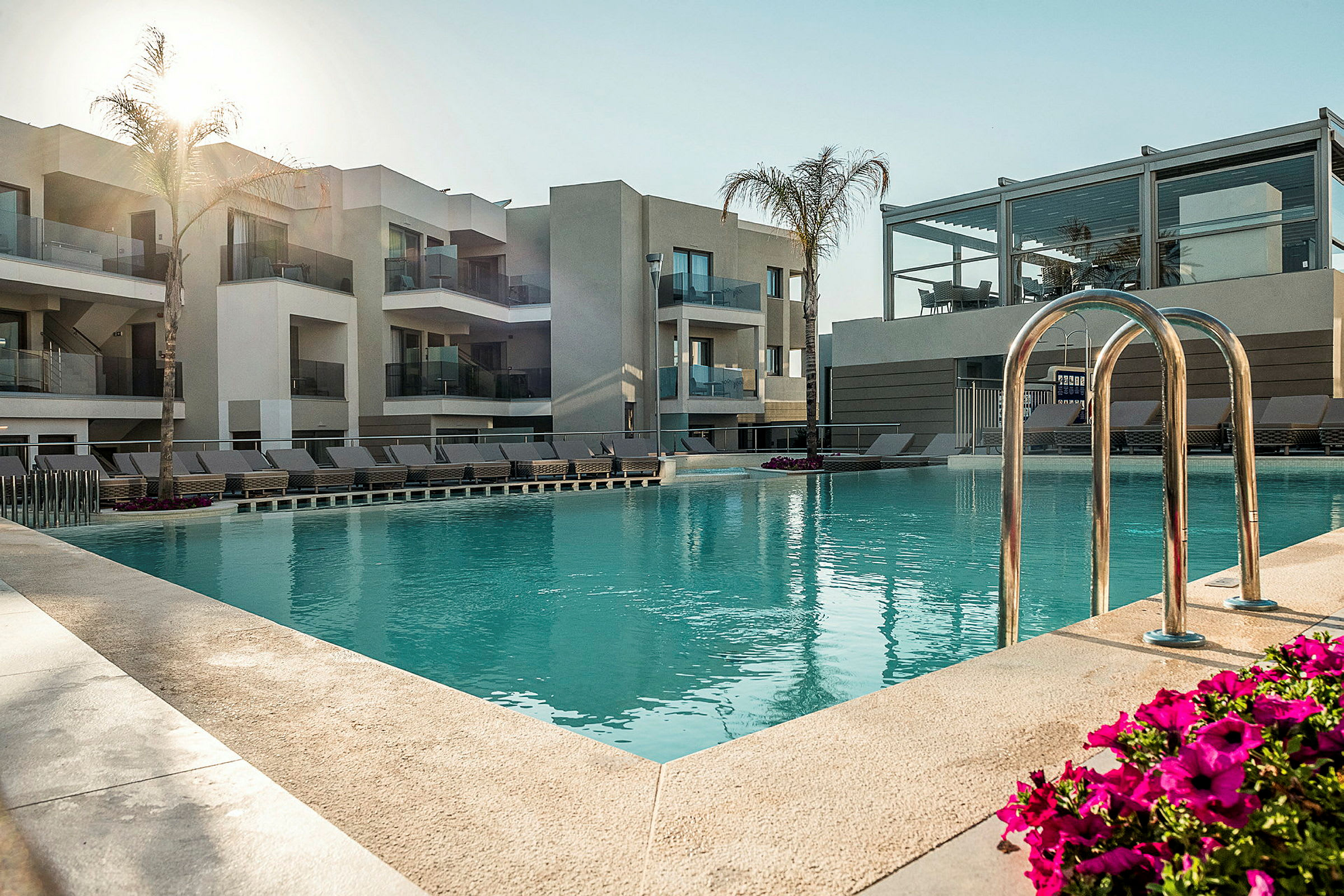 Udendørs pool ved et moderne hotel med liggestole og bygninger i baggrunden. (AI-genereret tekst)