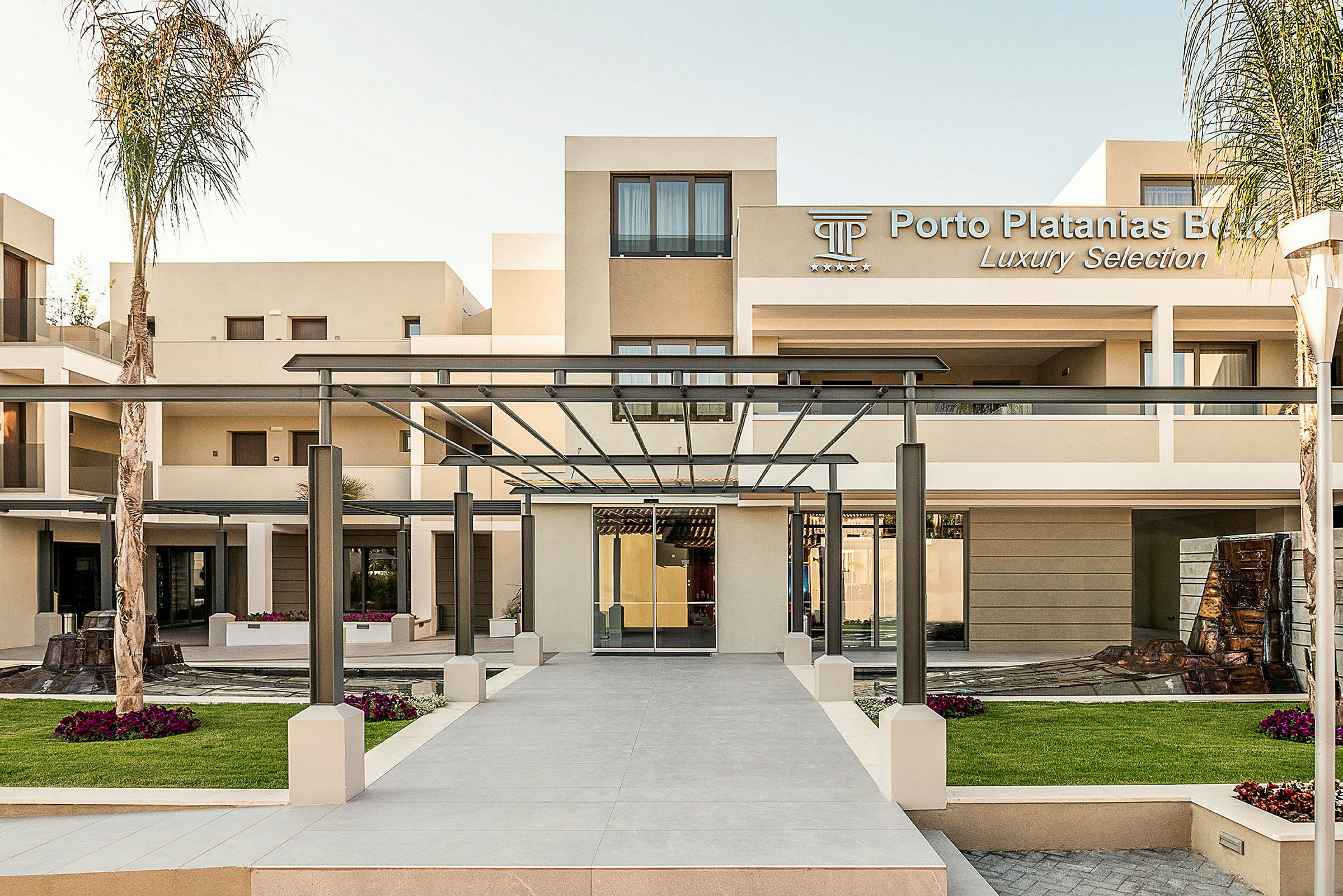Indgang til Porto Platanias Beach Resort med moderne bygninger og en pergola. (AI-genereret tekst)
