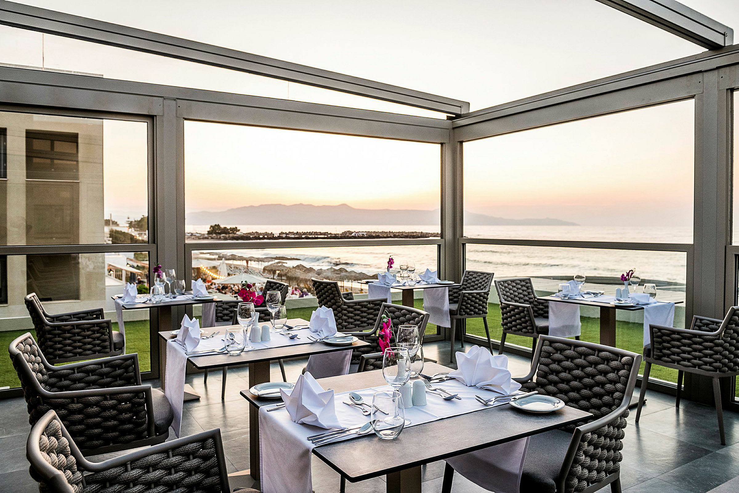 Et restaurantområde med dækkede borde og udsigt over havet ved solnedgang. (AI-genereret tekst)
