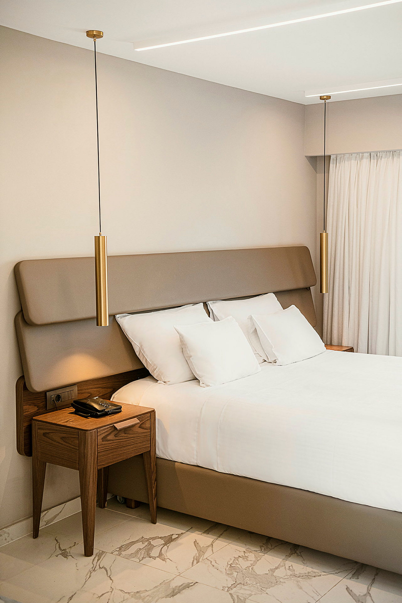 Et moderne og stilfuldt hotelværelse med en seng, træbord og hængende lamper. (AI-genereret tekst)
