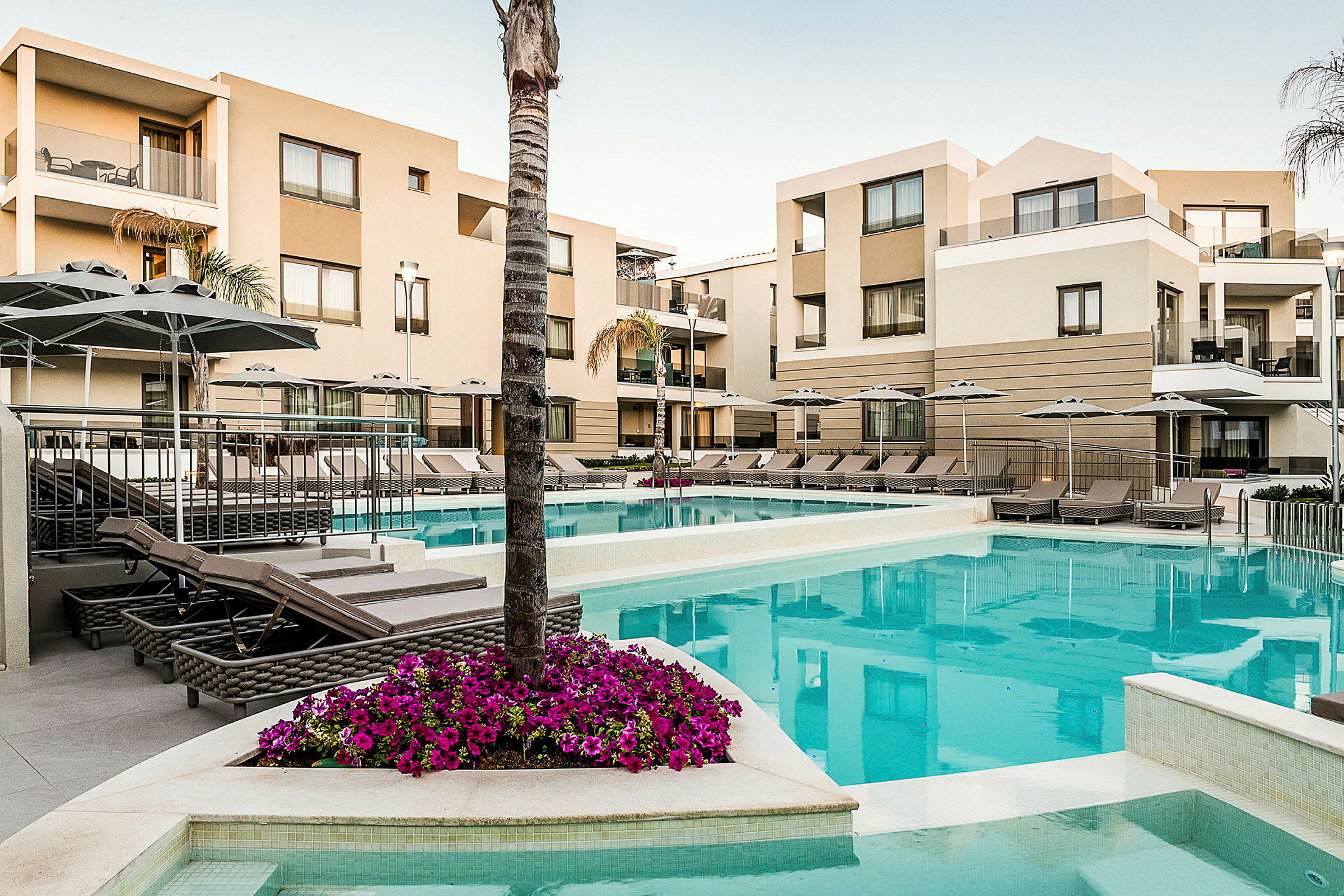 Billede af hotelkompleks med pool og liggestole, omgivet af moderne bygninger. (AI-genereret tekst)