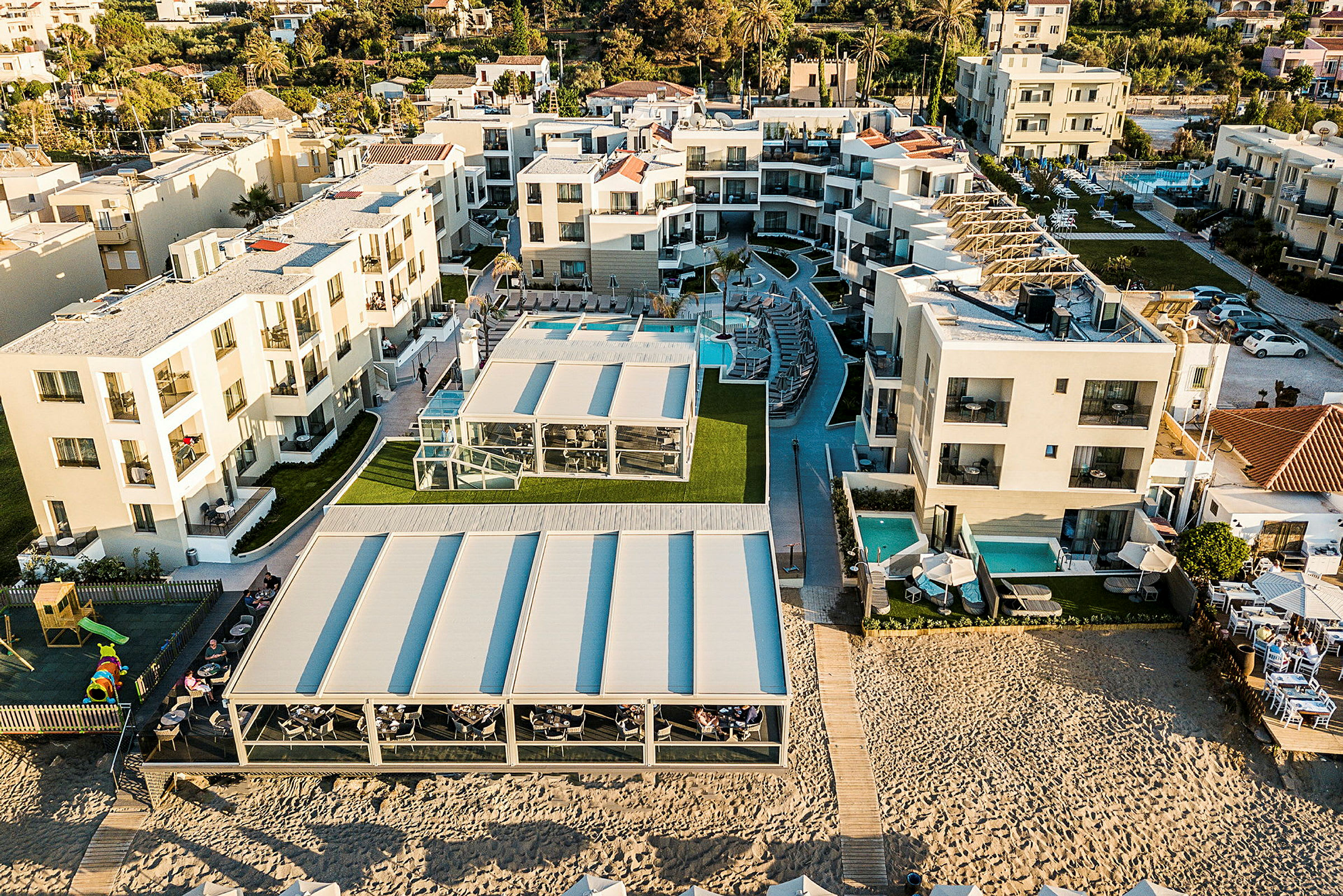 Luftfoto af hotelområde med moderne bygninger, pools og udendørsområder nær sandstrand. (AI-genereret tekst)