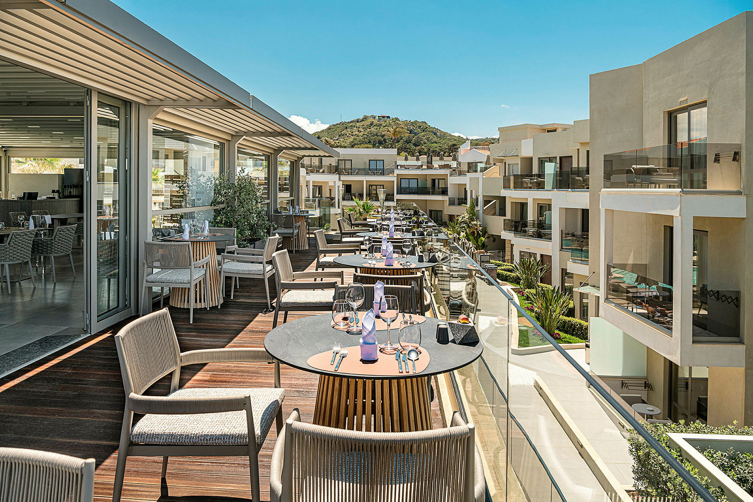 En terrasse med borde og stole med udsigt over moderne bygninger og grønne områder. (AI-genereret tekst)