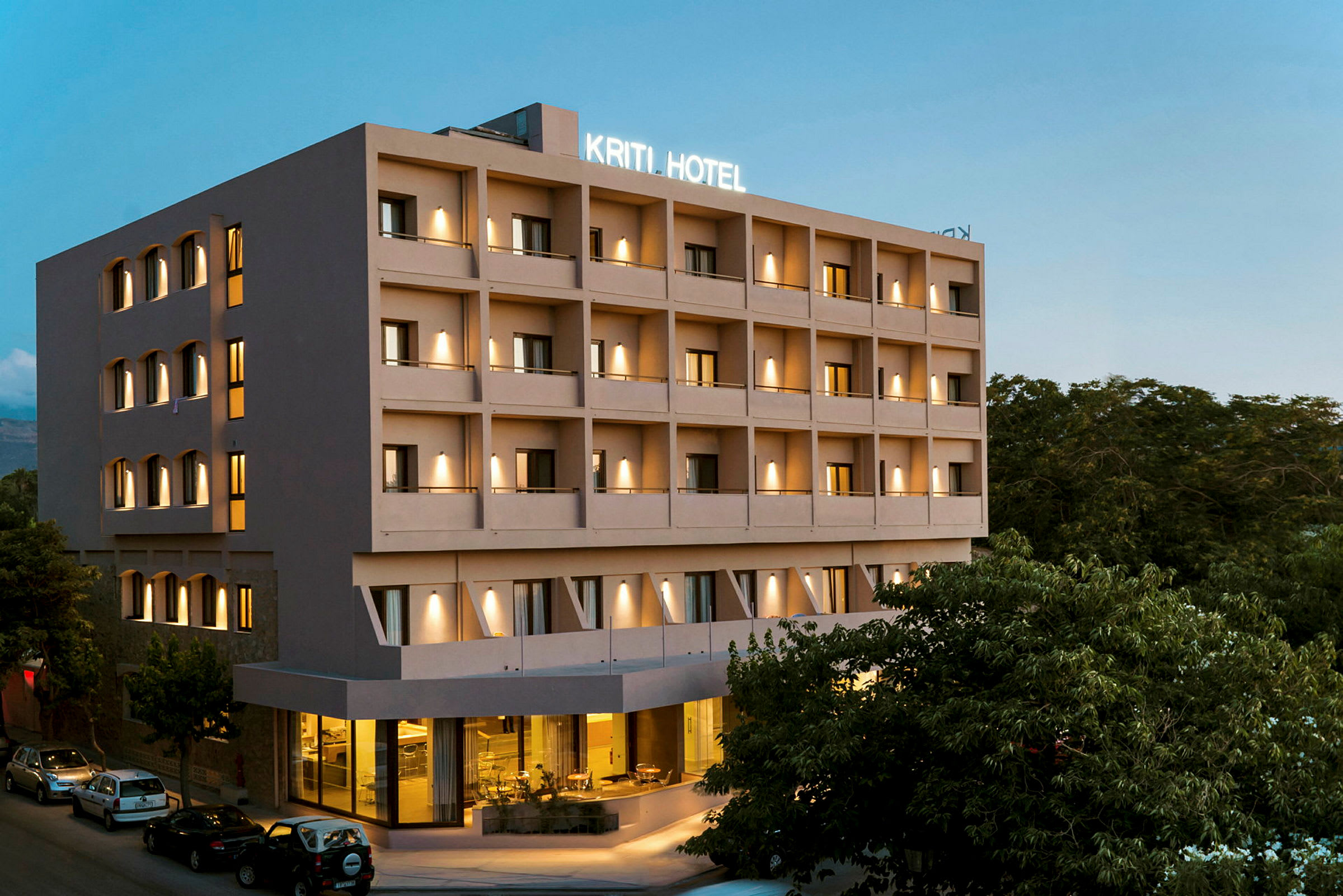 Hotelbygning med flere etager, belysning og parkering ved indgangen. (AI-genereret tekst)