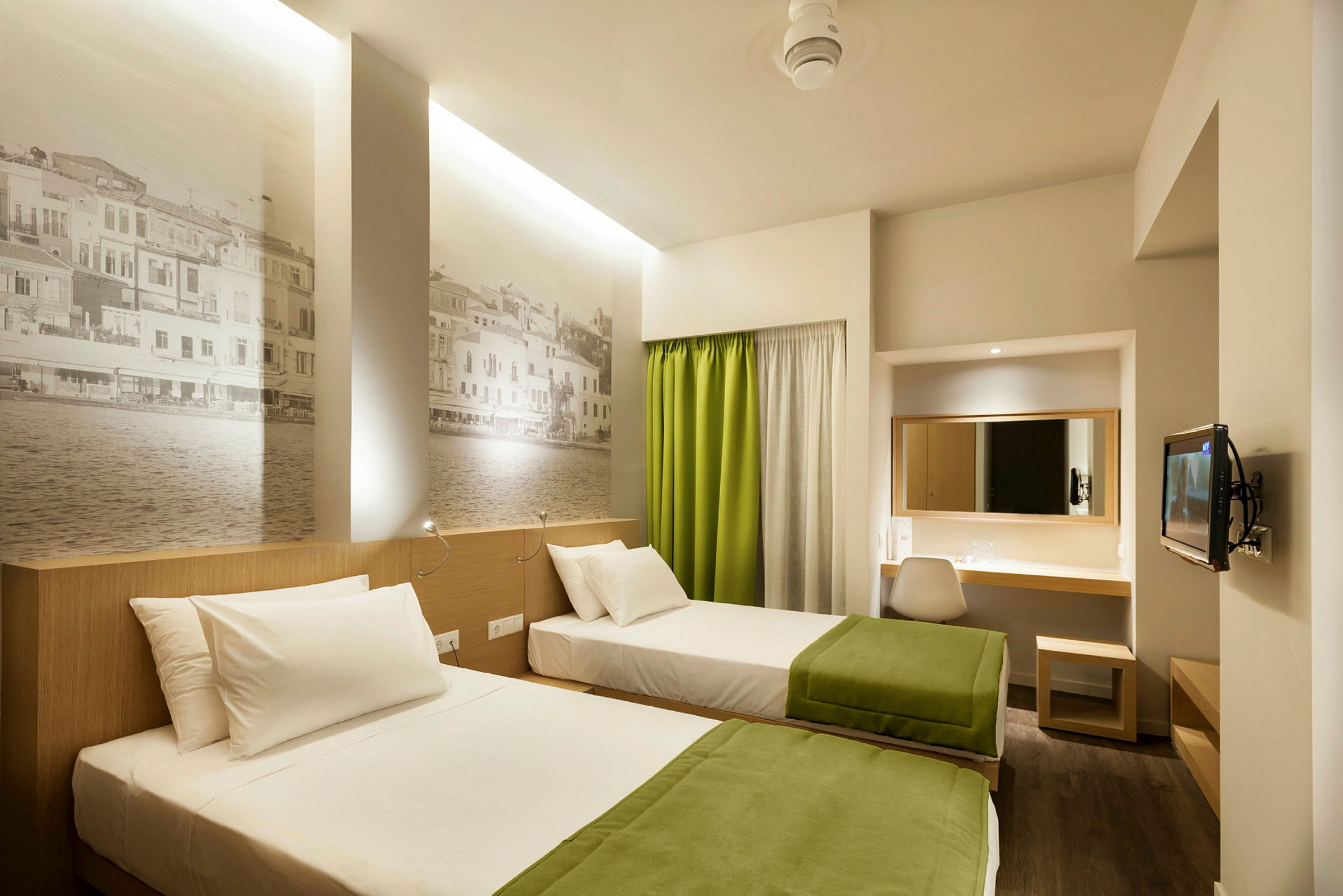 To enkeltsenge med grønne tæpper i et moderne hotelværelse med vægmalerier og skrivebord. (AI-genereret tekst)