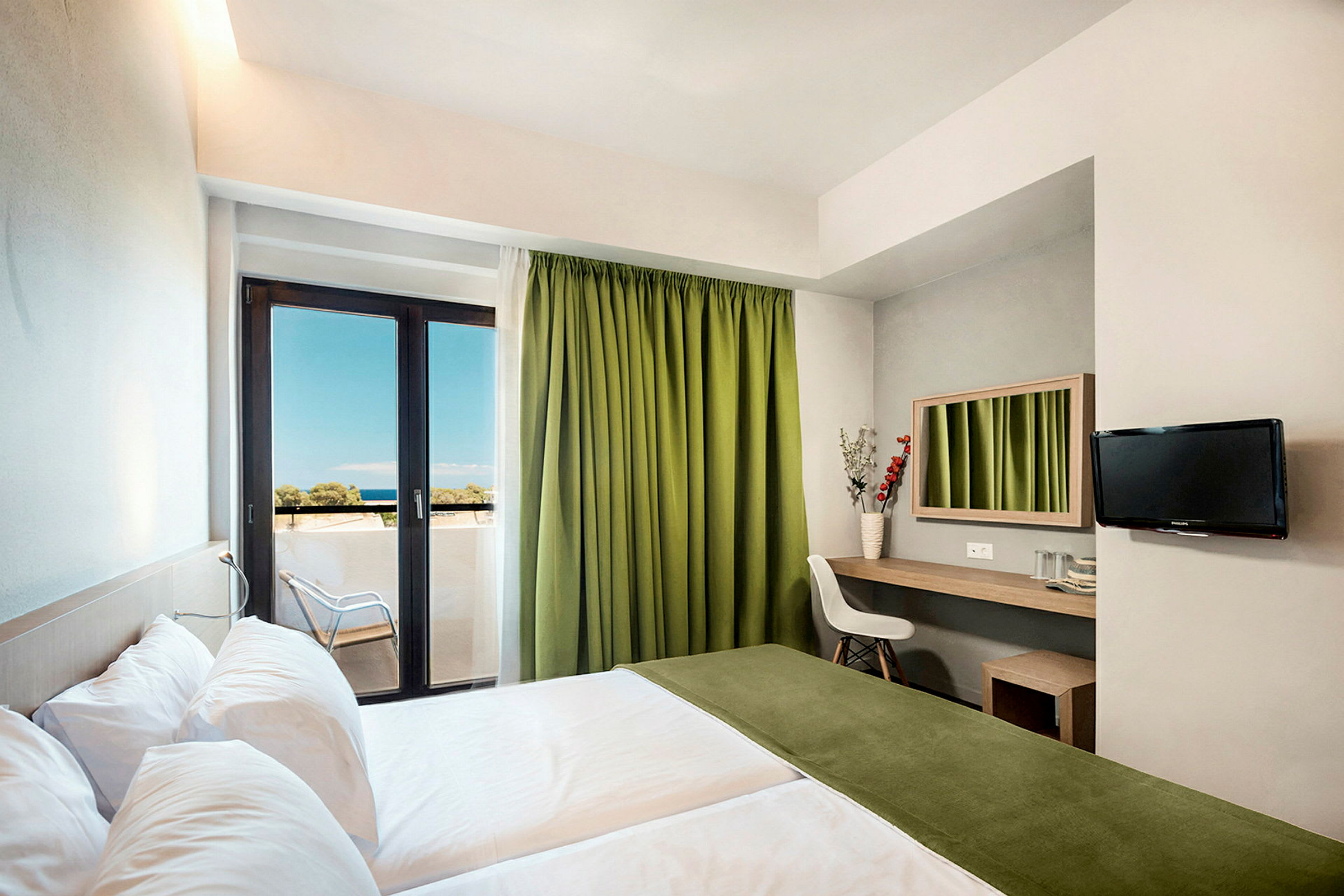 Et hotelværelse med to senge, en arbejdsplads med spejl, en stol og et tv på væggen. Værelset har en balkon med grønne gardiner og udsigt til havet. (AI-genereret tekst)