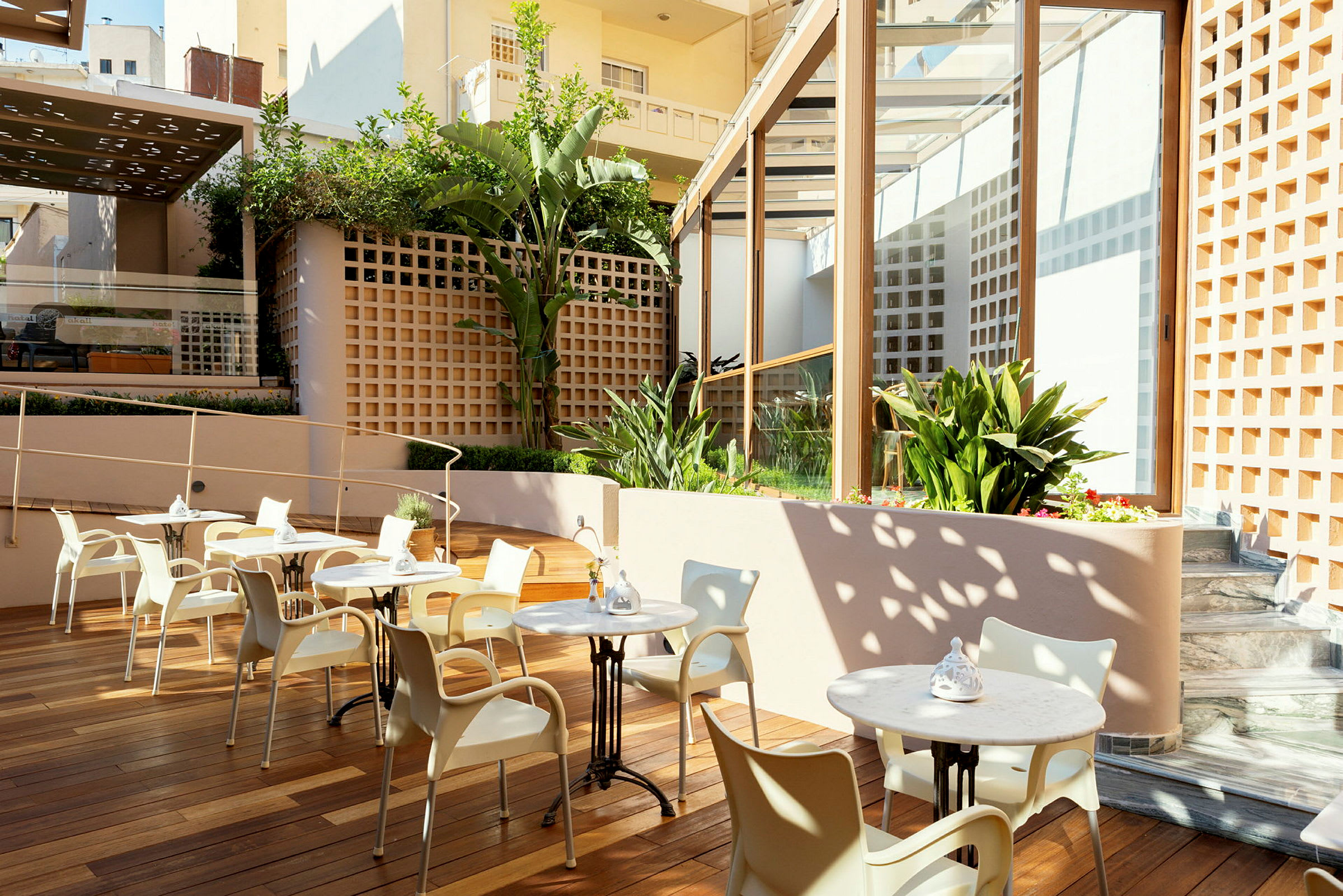 Billede af en terrasse med borde og stole, omgivet af planter og moderne arkitektur. (AI-genereret tekst)
