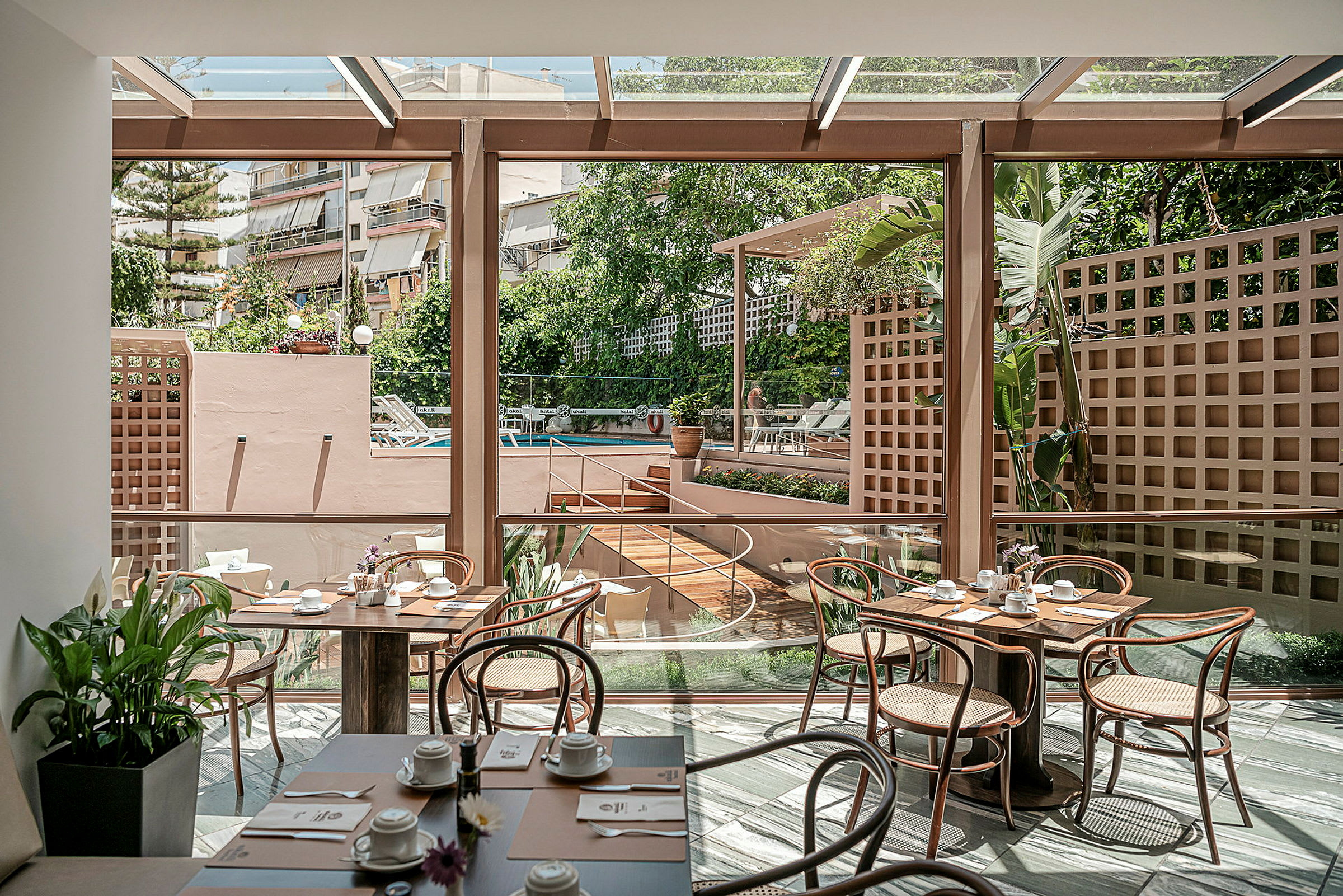 Interiør af en lys restaurant med glasvægge og udsigt over et udendørs poolområde. (AI-genereret tekst)