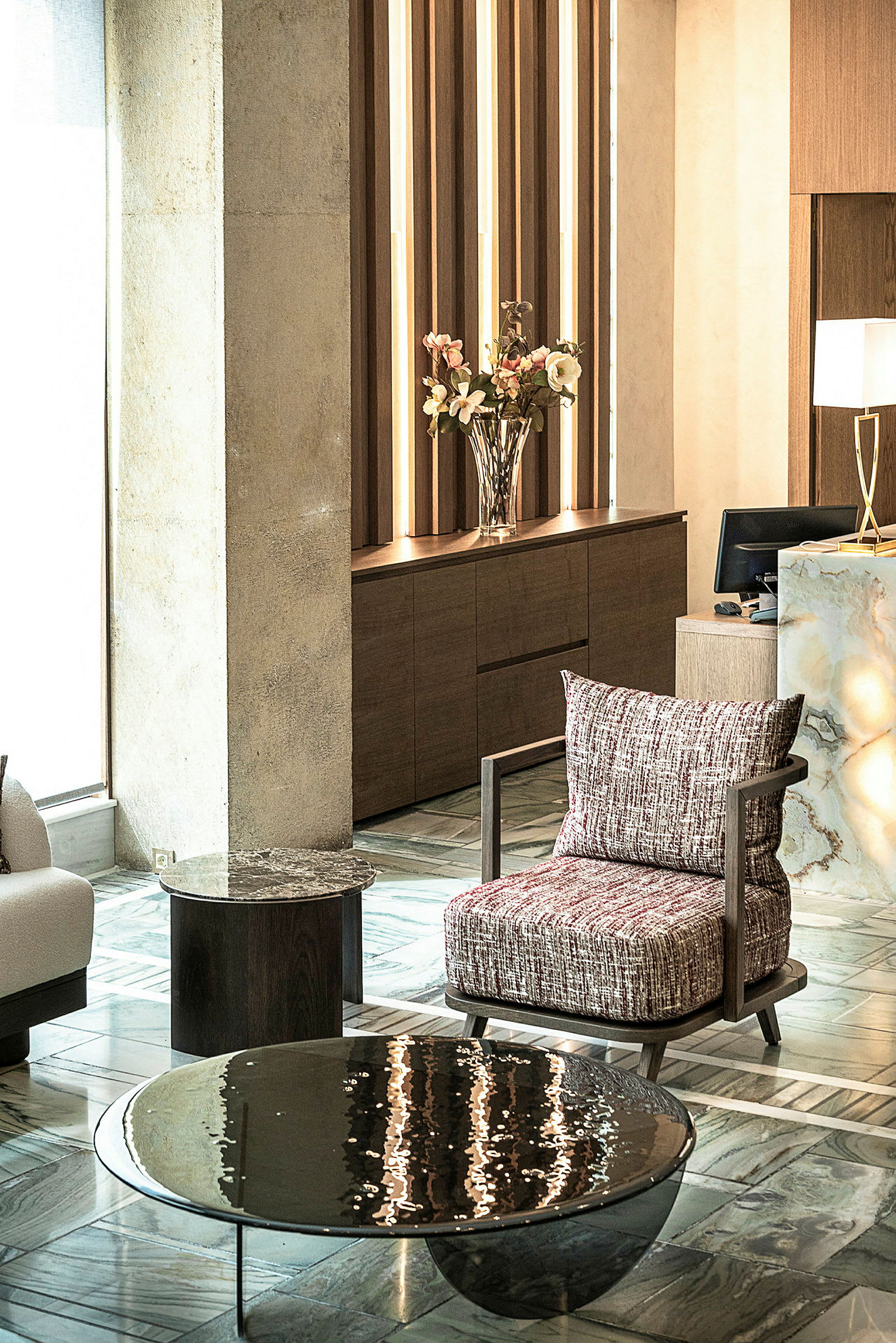 En hotellobby med moderne møbler, inklusive en polstret stol, sofabord og en vase med blomster. (AI-genereret tekst)