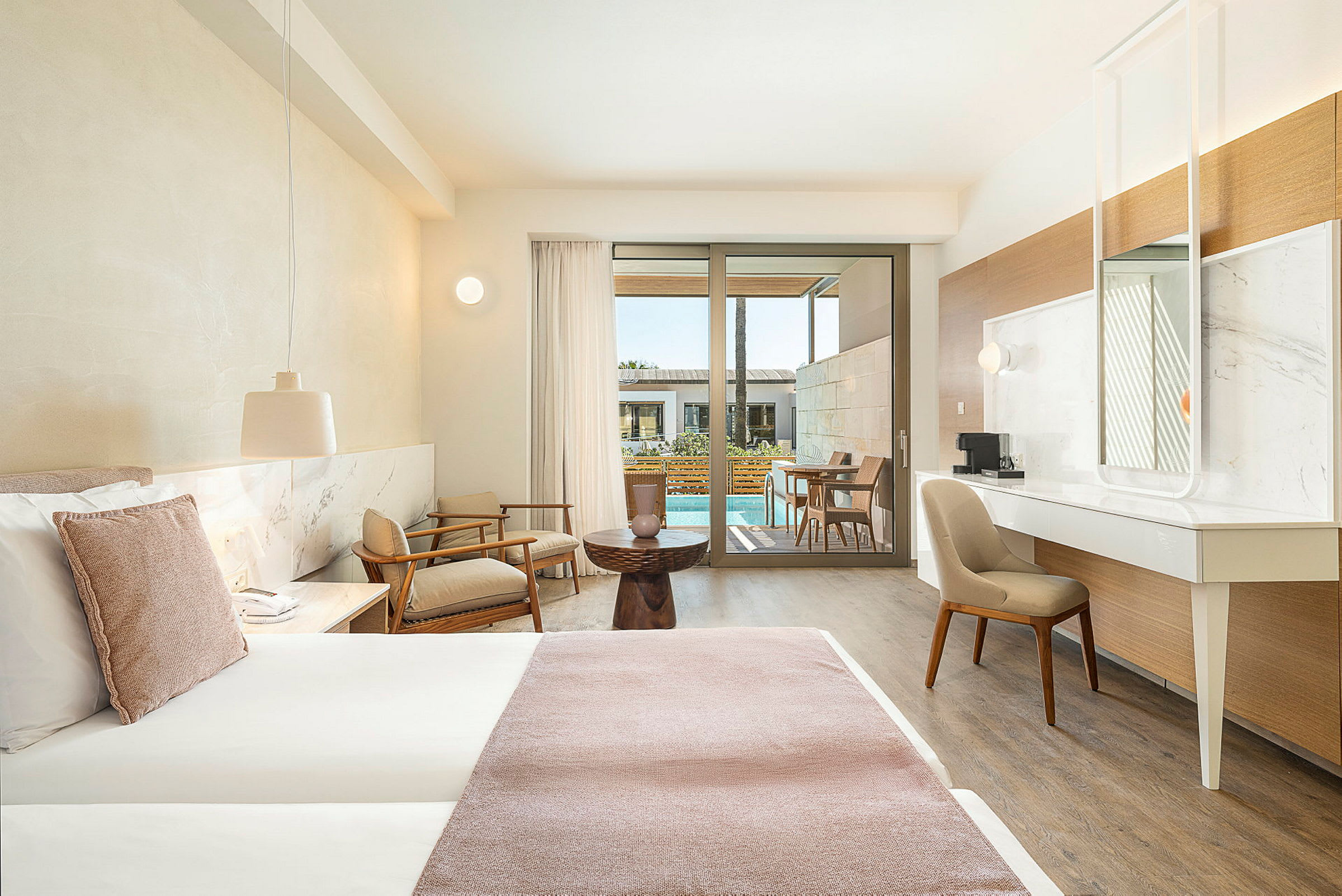Et hotelværelse med moderne indretning, en stor seng, siddeområde og udsigt til en terrasse med pool. (AI-genereret tekst)