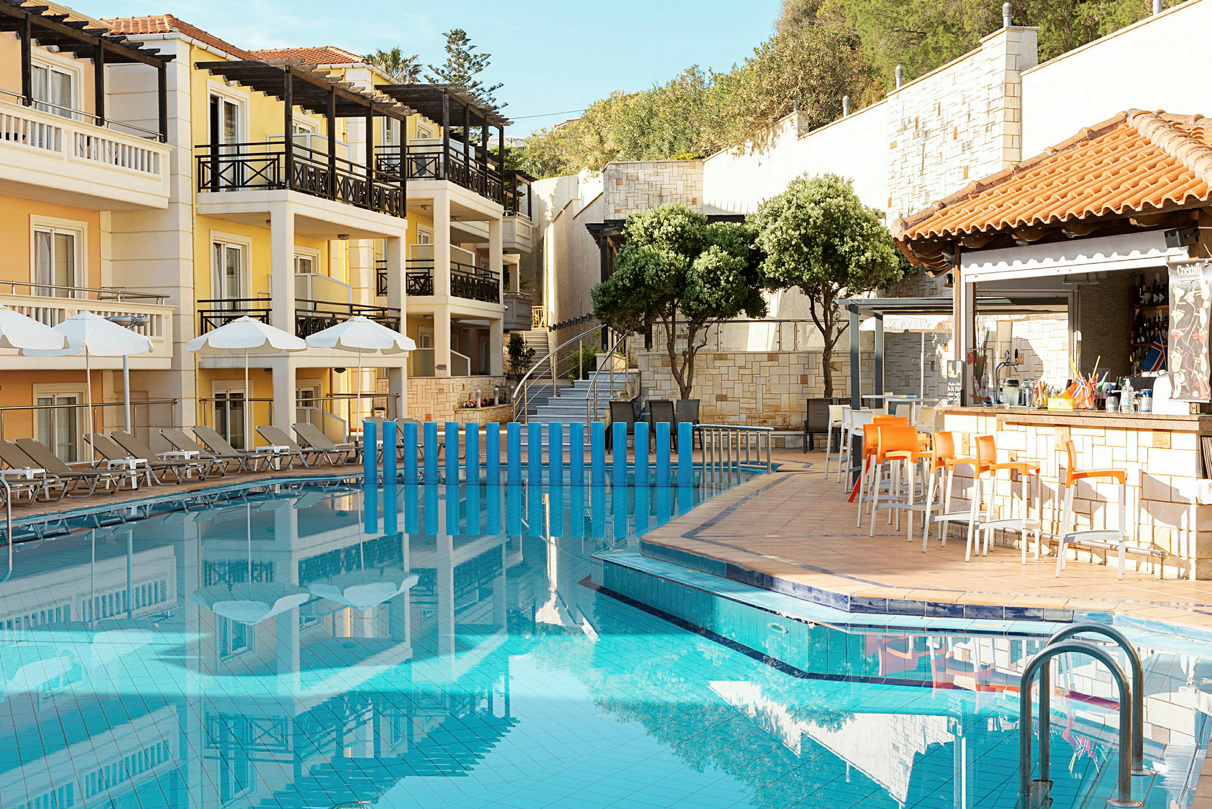 Billede af en hotelpool med liggestole og parasoller på siden samt en bar med stole. (AI-genereret tekst)