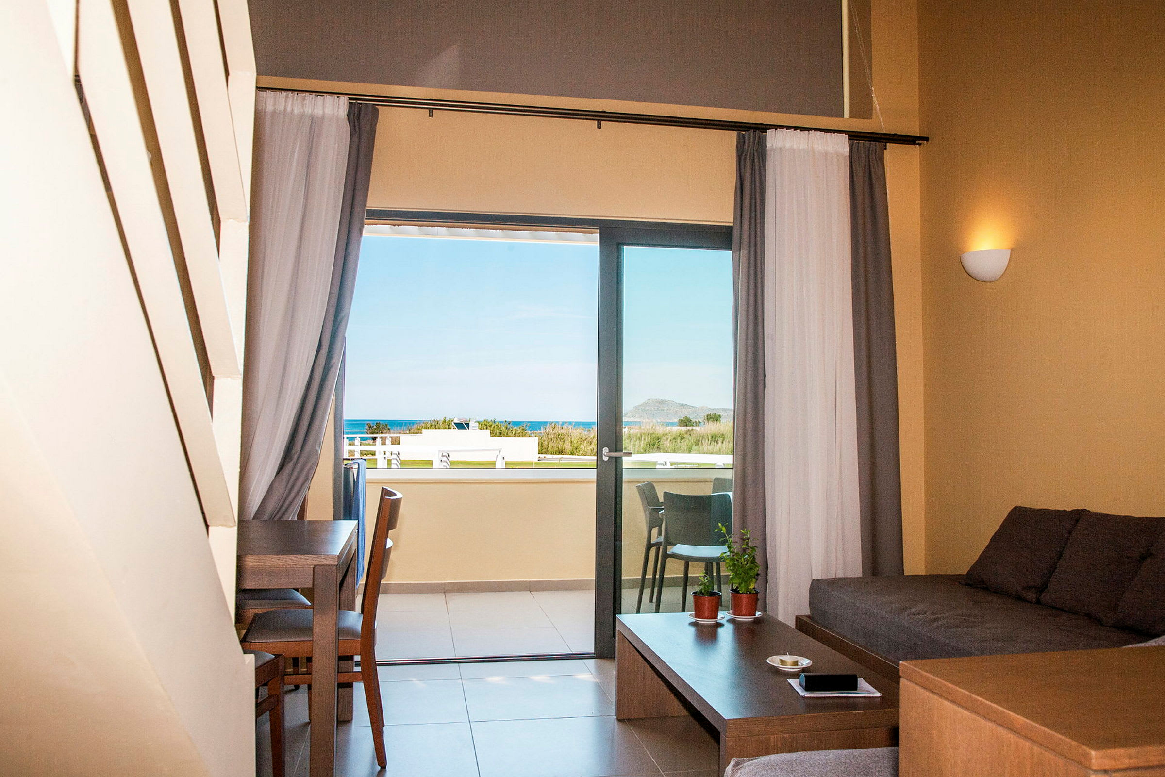 Udsigt fra et hotelværelse med siddeområde og balkon, hvor man kan se havet. (AI-genereret tekst)