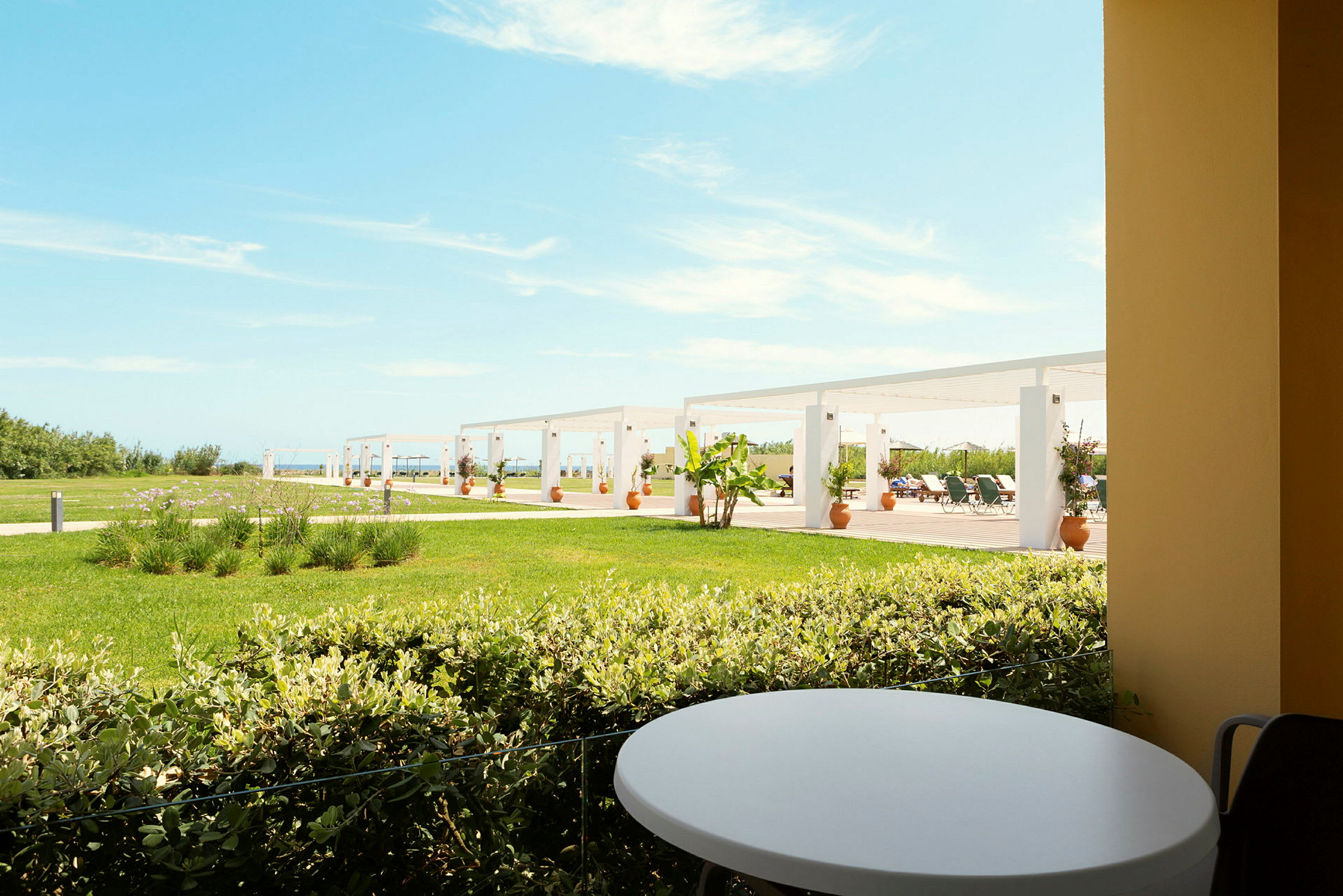 Udsigt fra en terrasse med et rundt bord mod en græsplæne og pergola i baggrunden. (AI-genereret tekst)