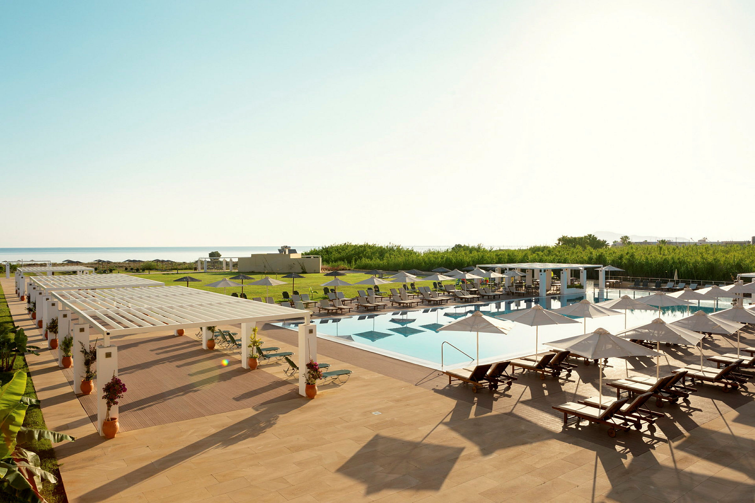 En udendørs pool med liggestole og parasoller på et hotelområde ved havet. (AI-genereret tekst)