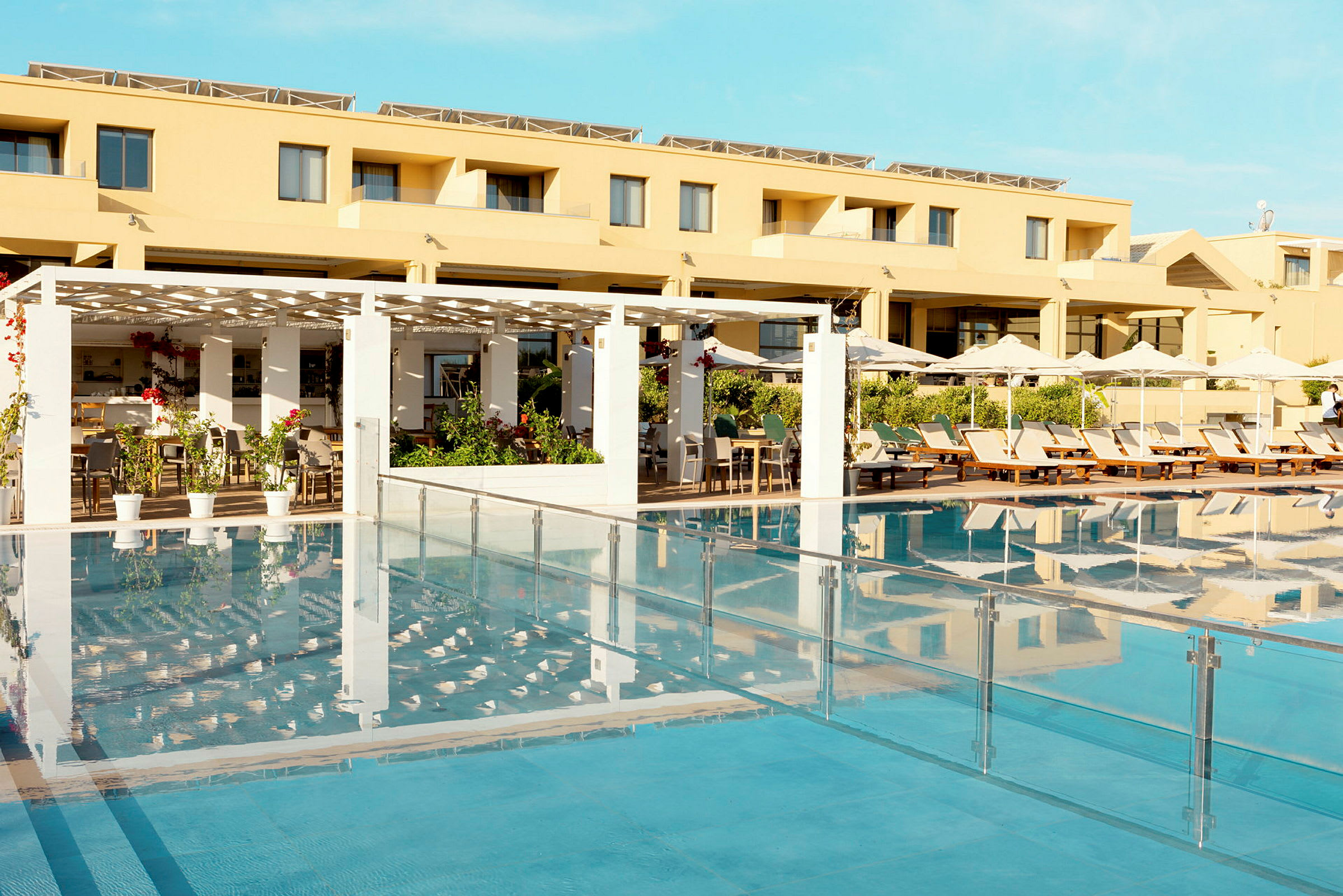 Hotellets facade med pool og liggestole i forgrunden. (AI-genereret tekst)