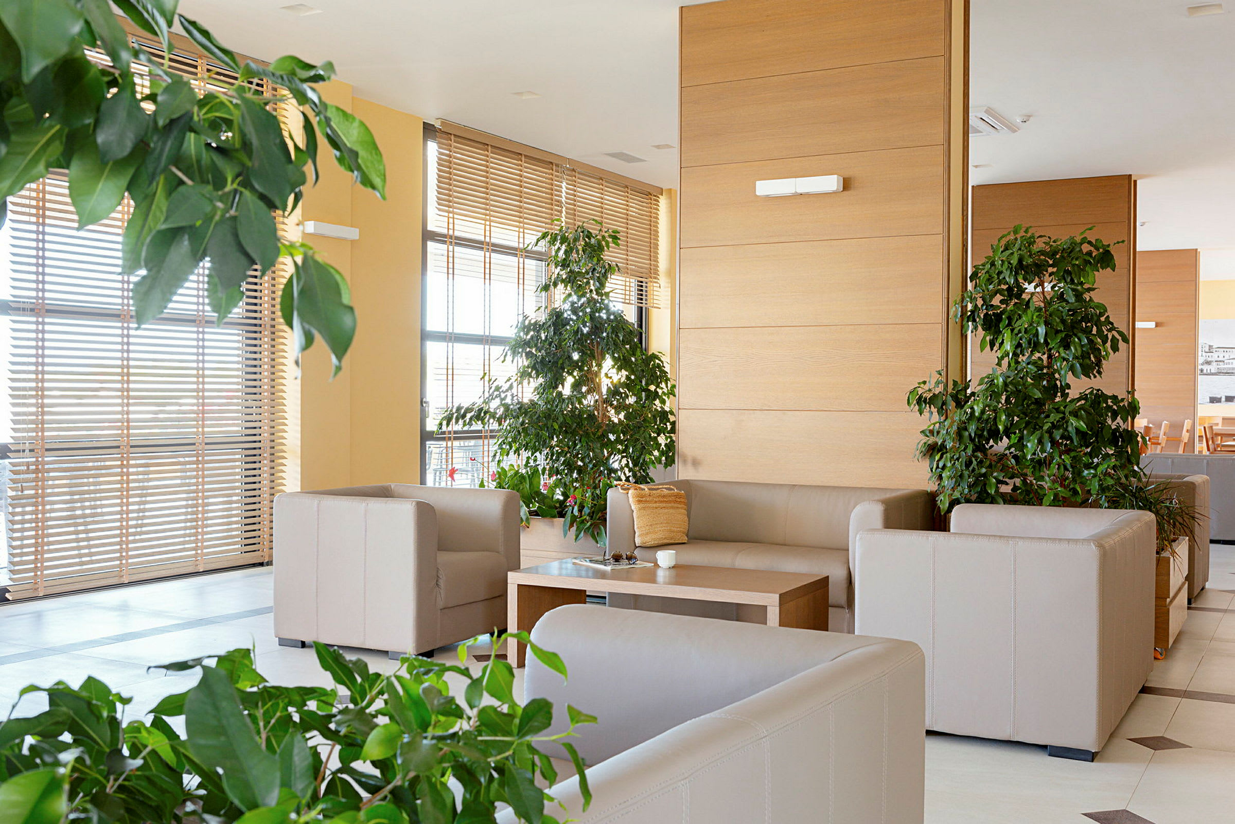 Billede af en moderne og lys stue med beige sofaer, et træbord og grønne planter. (AI-genereret tekst)