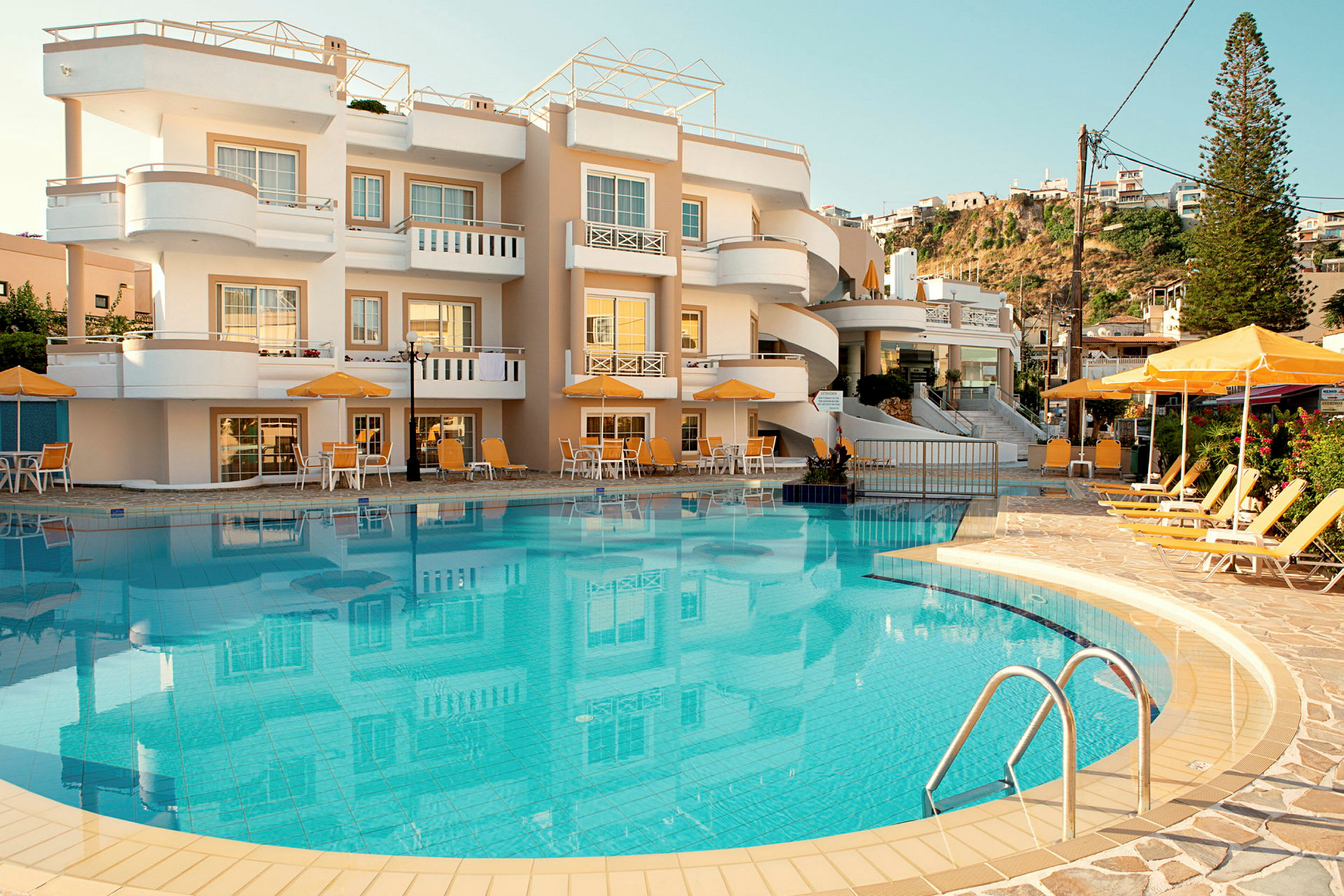 Billede af et hotel med en pool og liggestole foran bygningen. (AI-genereret tekst)