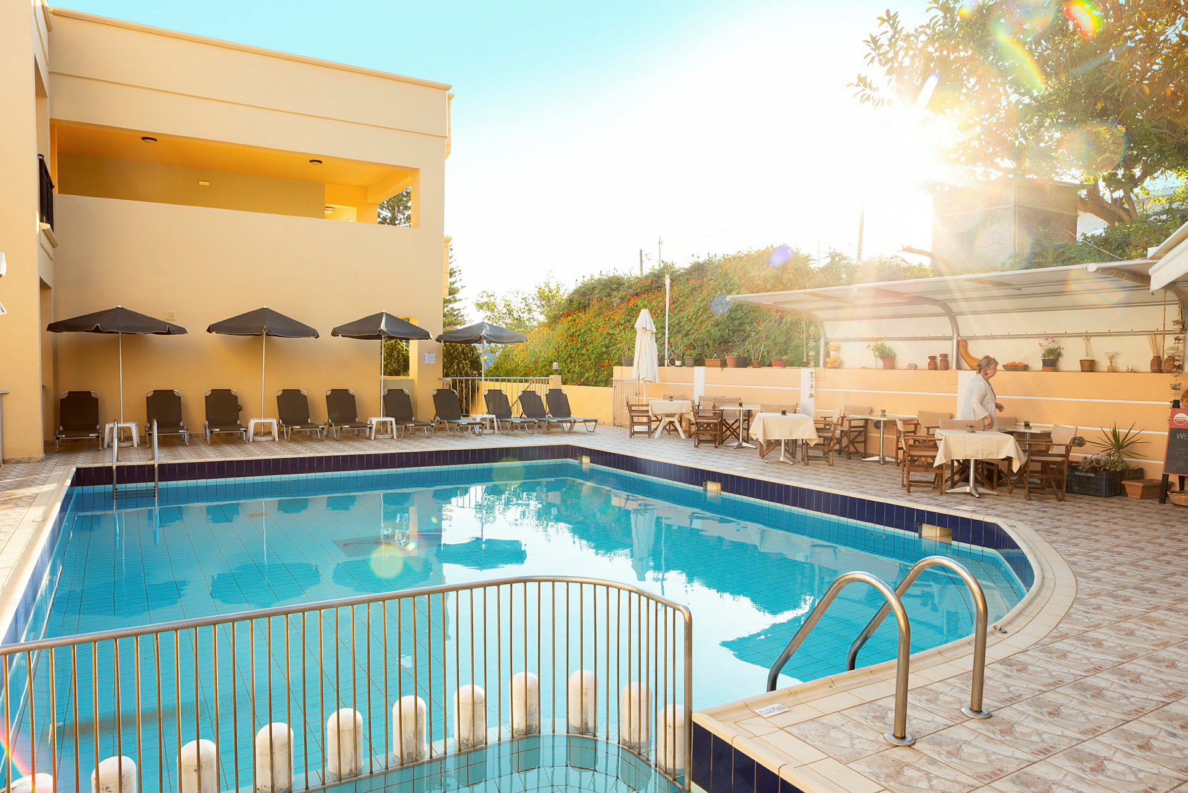 En pool ved et hotel med solsenge, parasoller og et spiseområde ved siden af. (AI-genereret tekst)