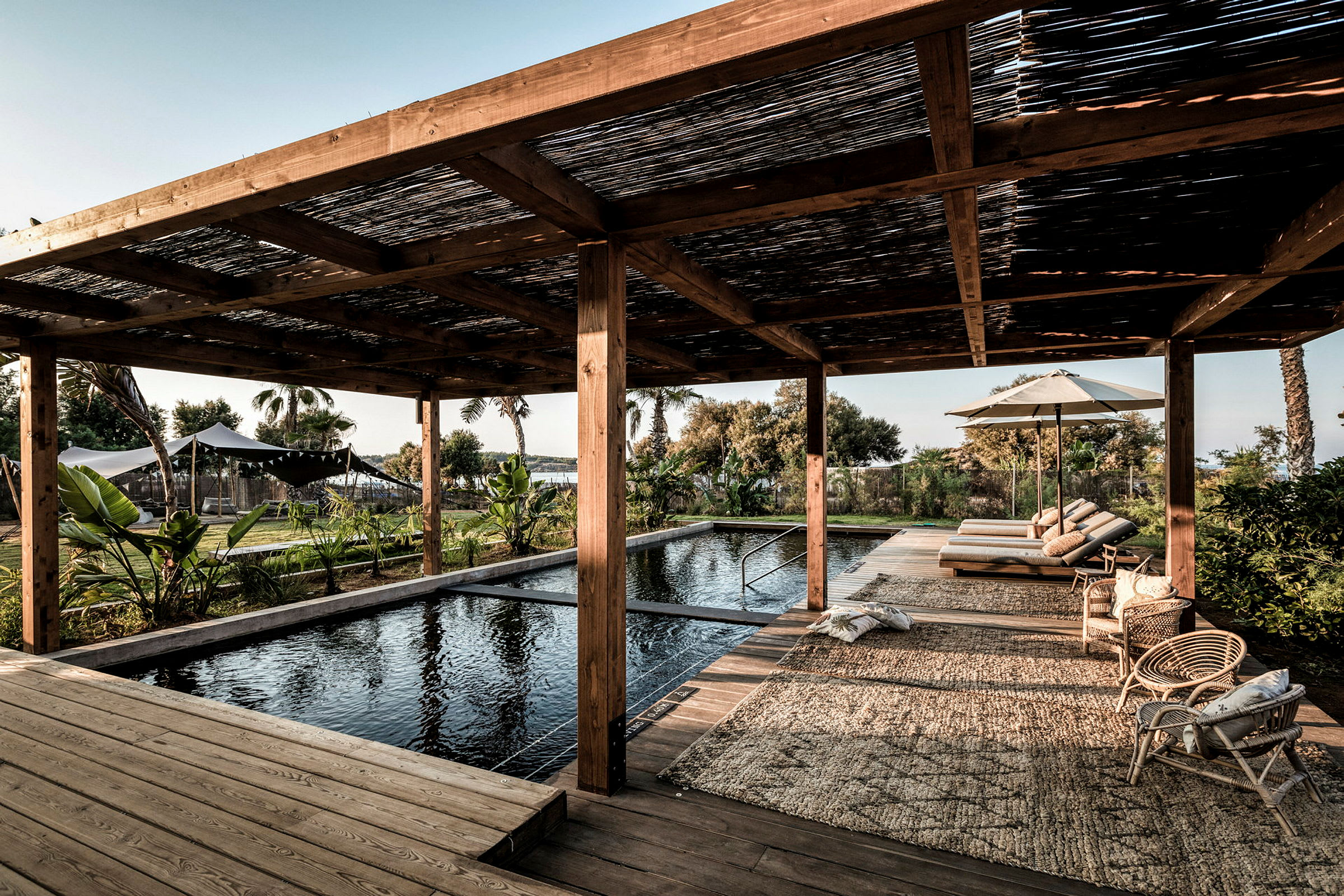 Pulserende pool under en træpergola med liggestole og frodige omgivelser. (AI-genereret tekst)