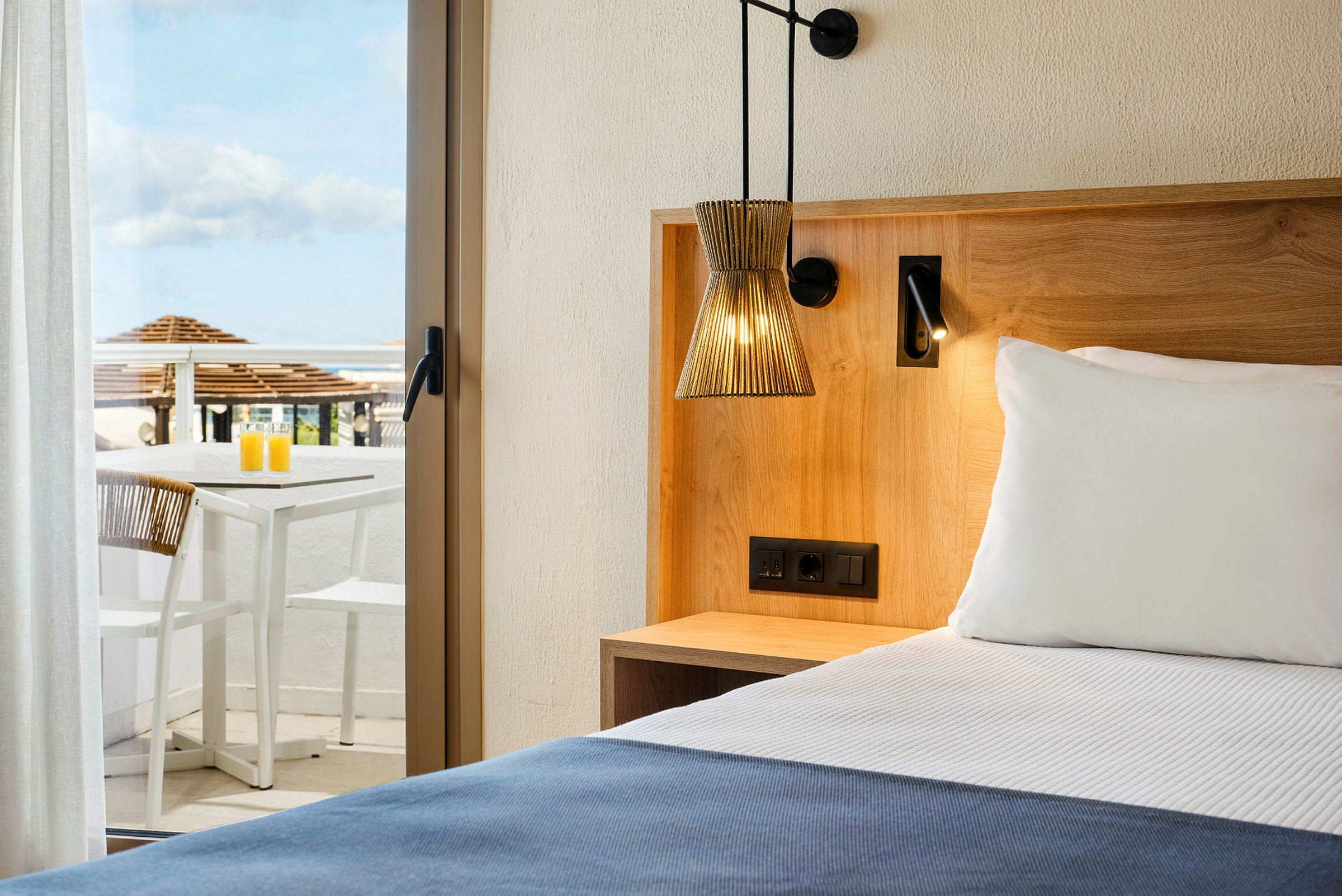Hotelværelse med en seng, træinteriør og en terrasse med bord og stole i baggrunden. (AI-genereret tekst)