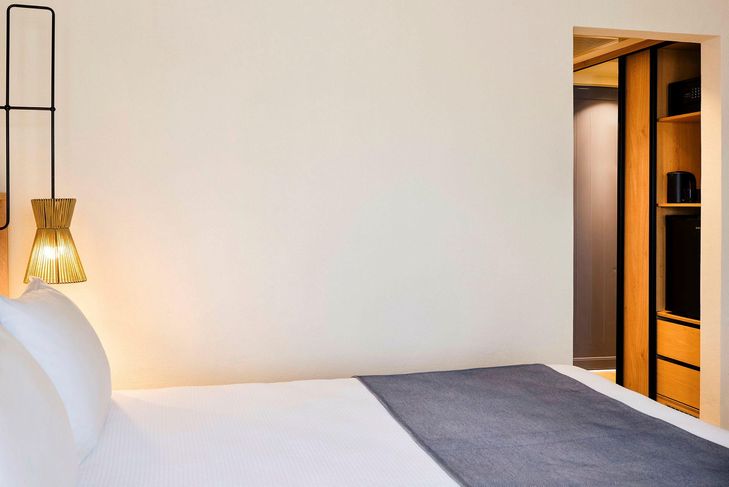 Et hotelværelse med en seng, en moderne lampe og en del af indretningen med opbevaringsplads. (AI-genereret tekst)