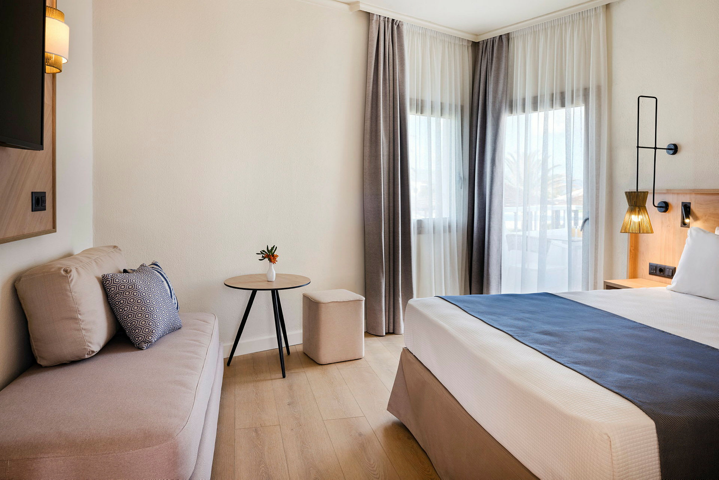 Et hotelværelse med en seng, sofa og bord ved siden af store vinduer. (AI-genereret tekst)