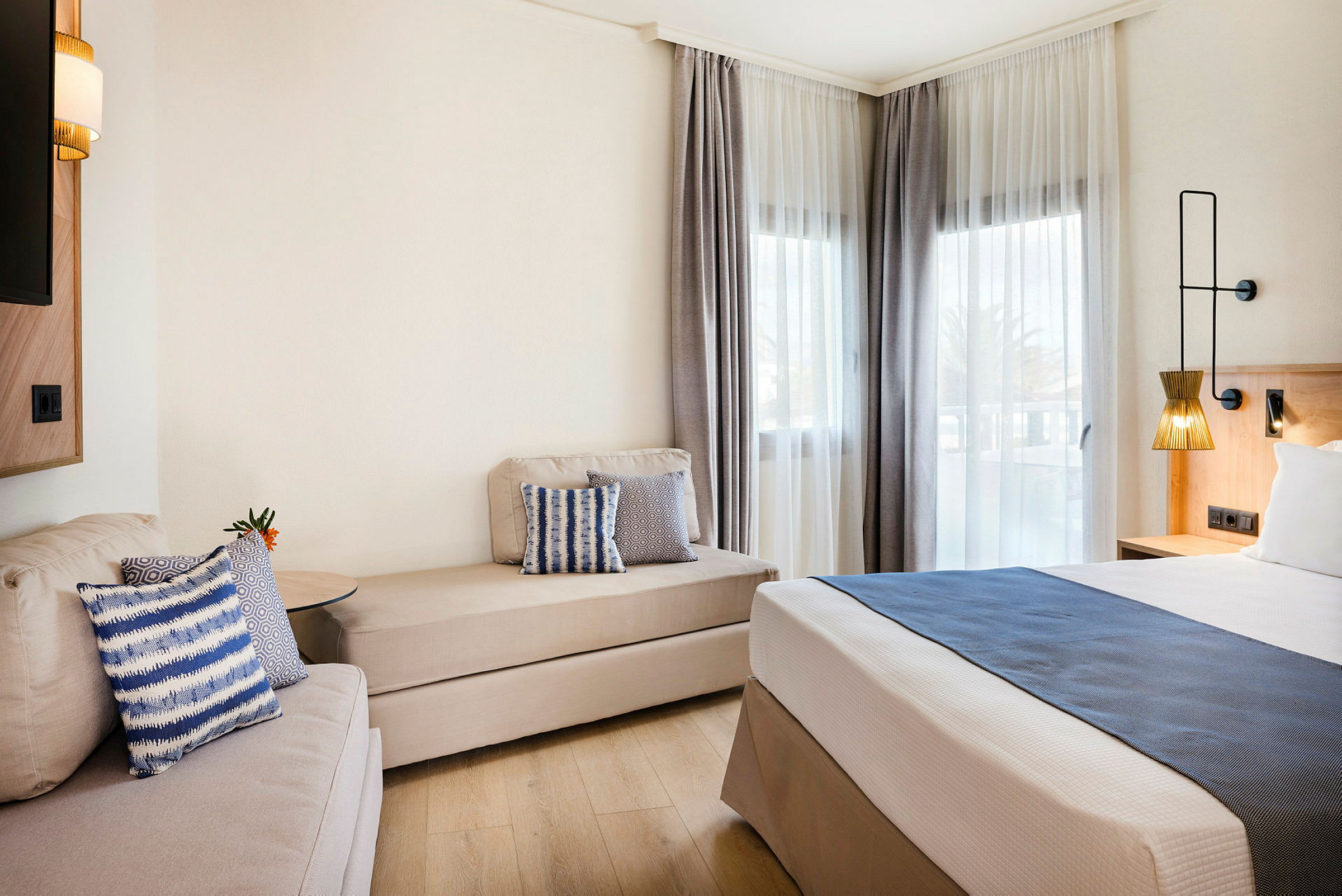 Moderne hotelværelse med seng, sofa og vinduer med lyse gardiner. (AI-genereret tekst)