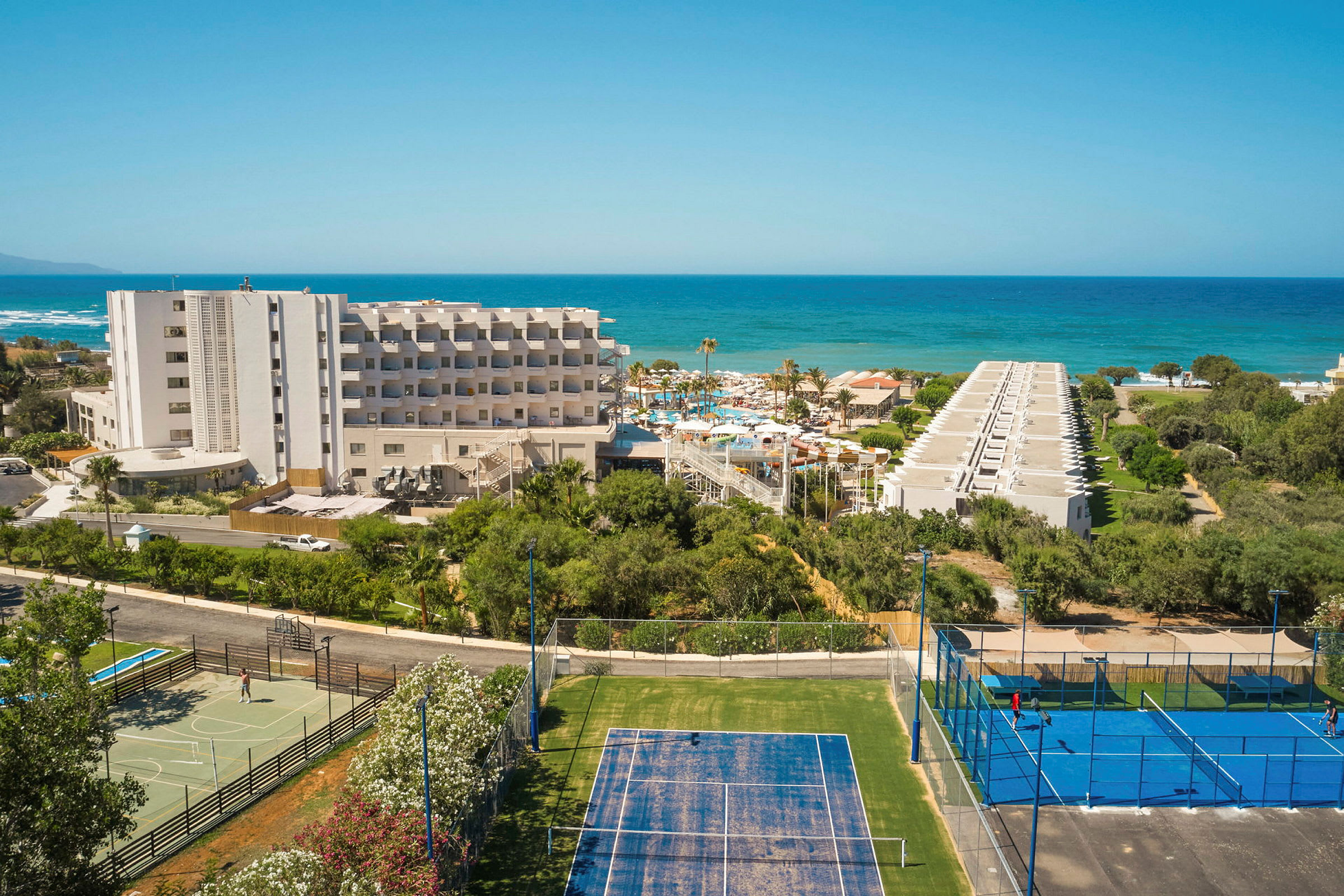 Hotelbygning med tennisbaner i forgrunden og havet i baggrunden. (AI-genereret tekst)