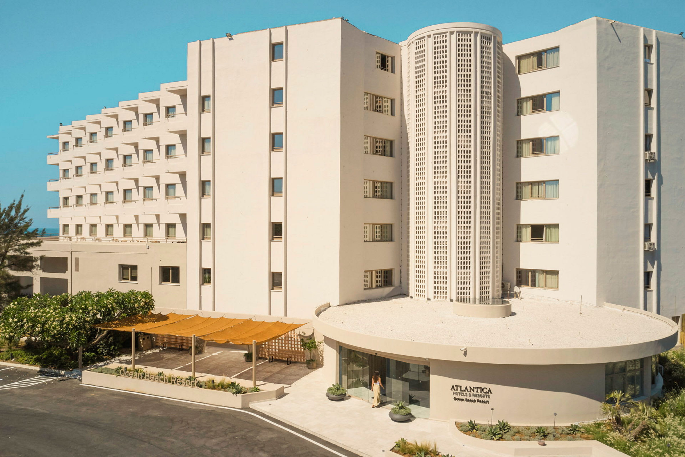 Hvidmoderne bygning med flere etager og hotellets navn synligt ved indgangen. (AI-genereret tekst)