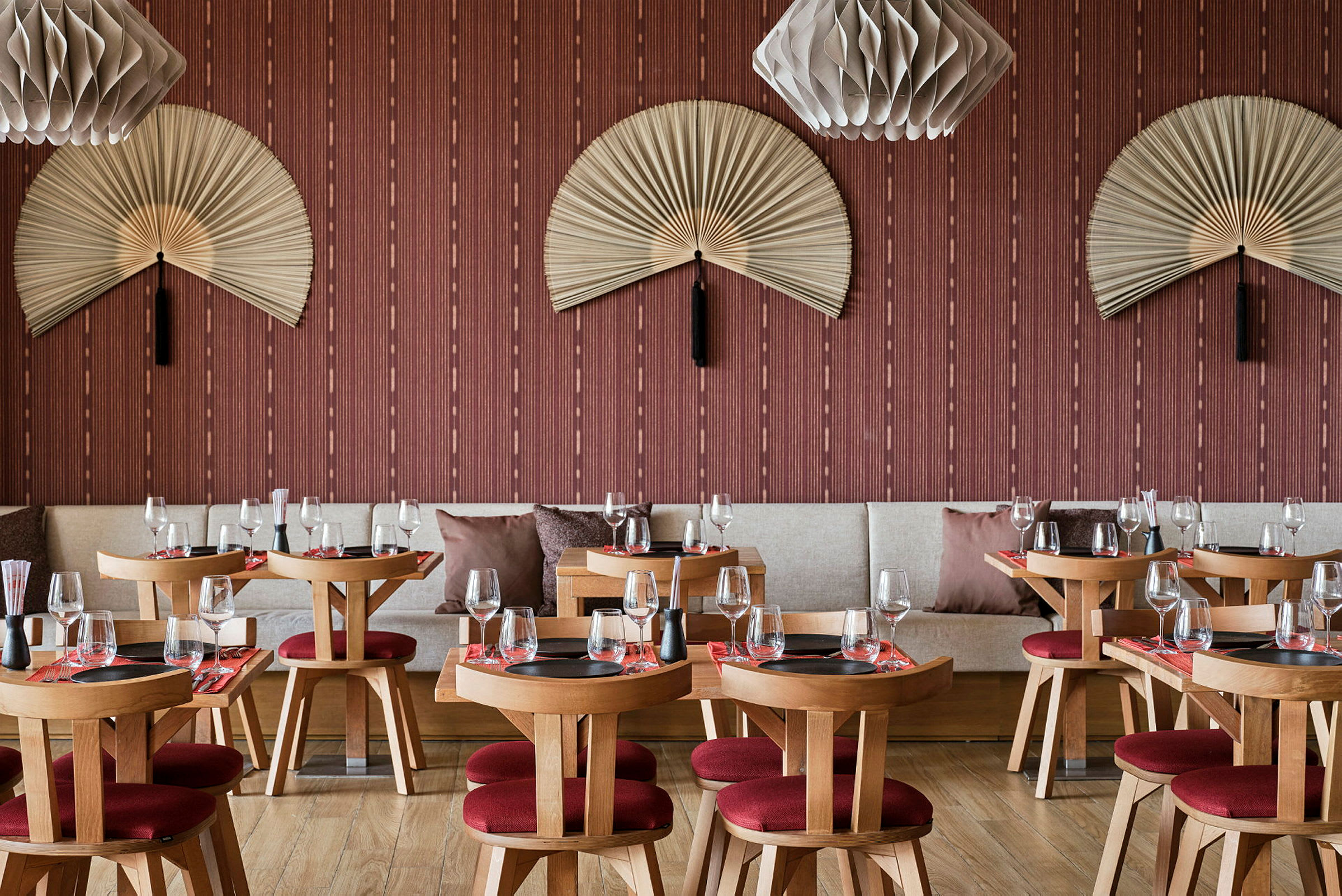 En restaurant med træborde og røde stole, dekoreret med væghængte vifter og moderne lamper. (AI-genereret tekst)