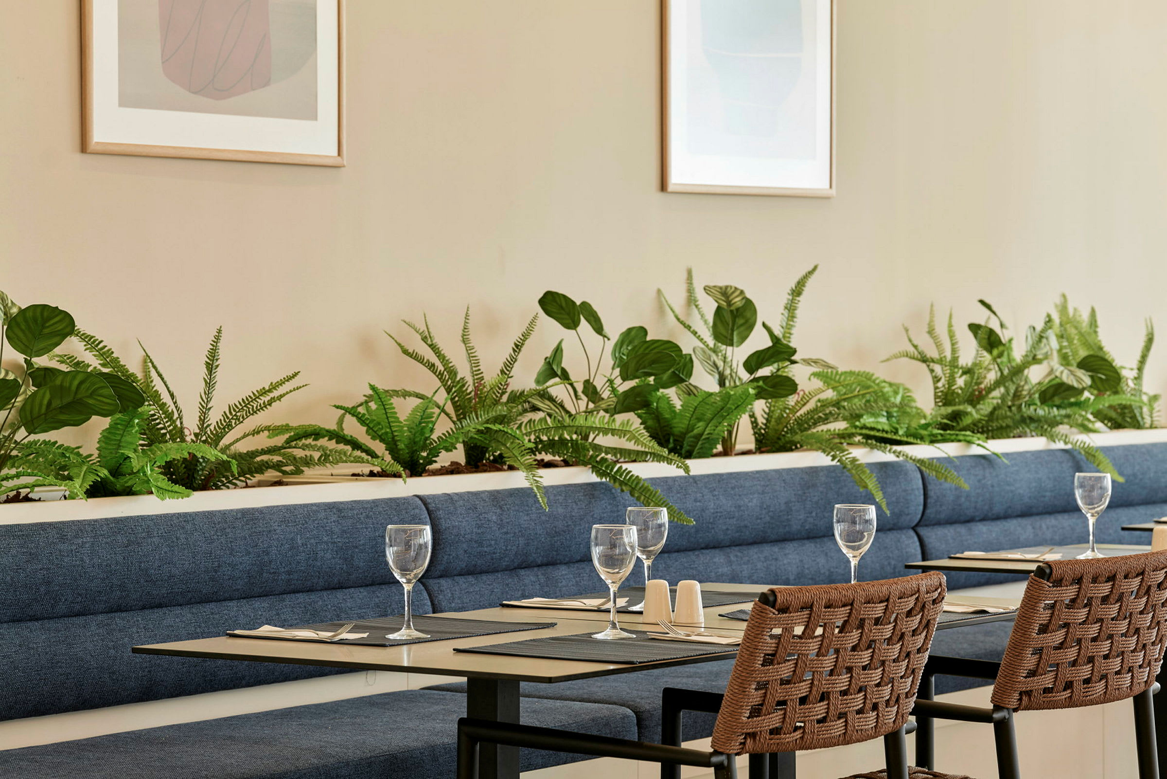 Et restaurantområde med blå sofaer, dekoreret med grønne planter og dækkede borde. (AI-genereret tekst)