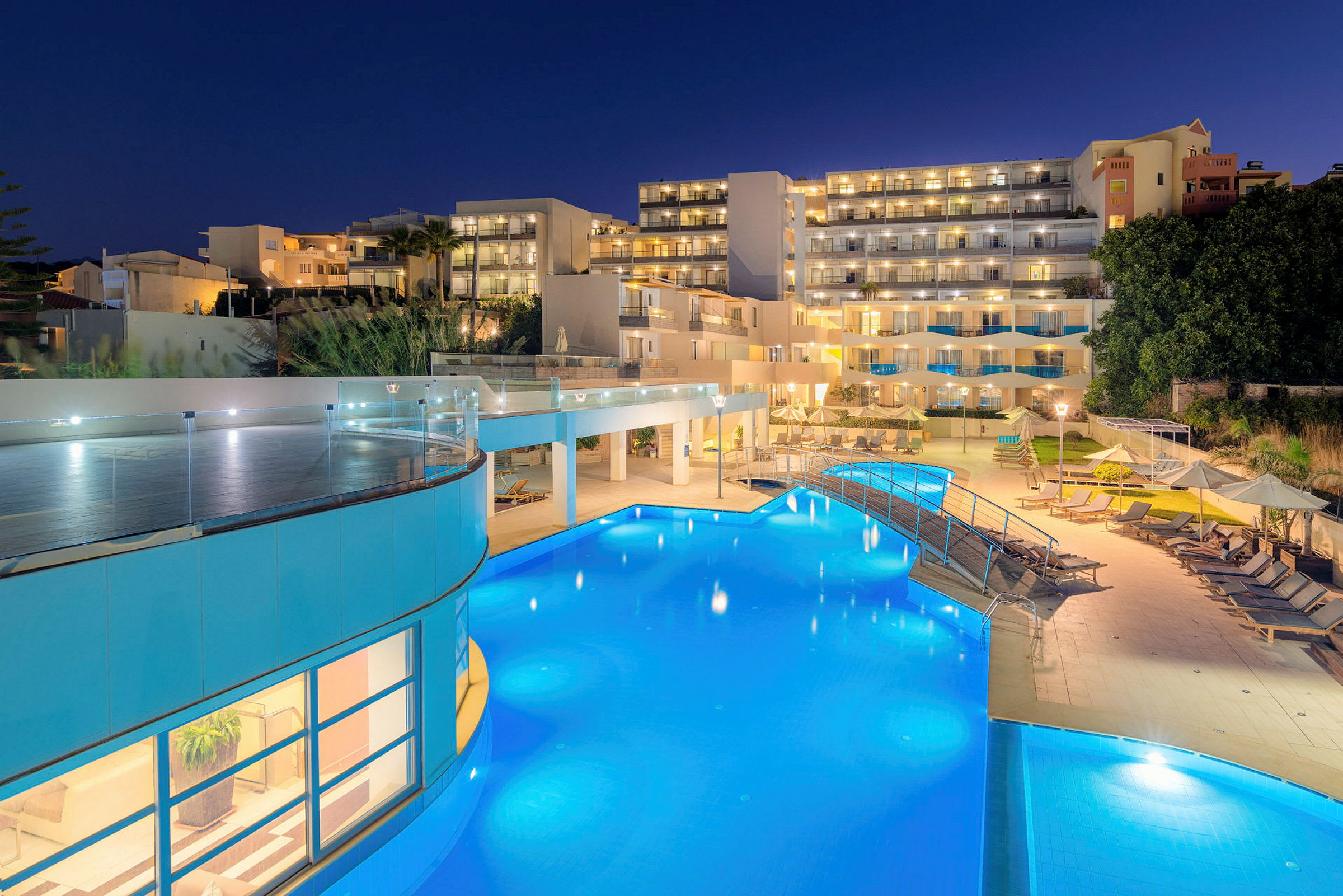 En hotelbygning med oplyste altaner og en udendørs pool om aftenen. (AI-genereret tekst)