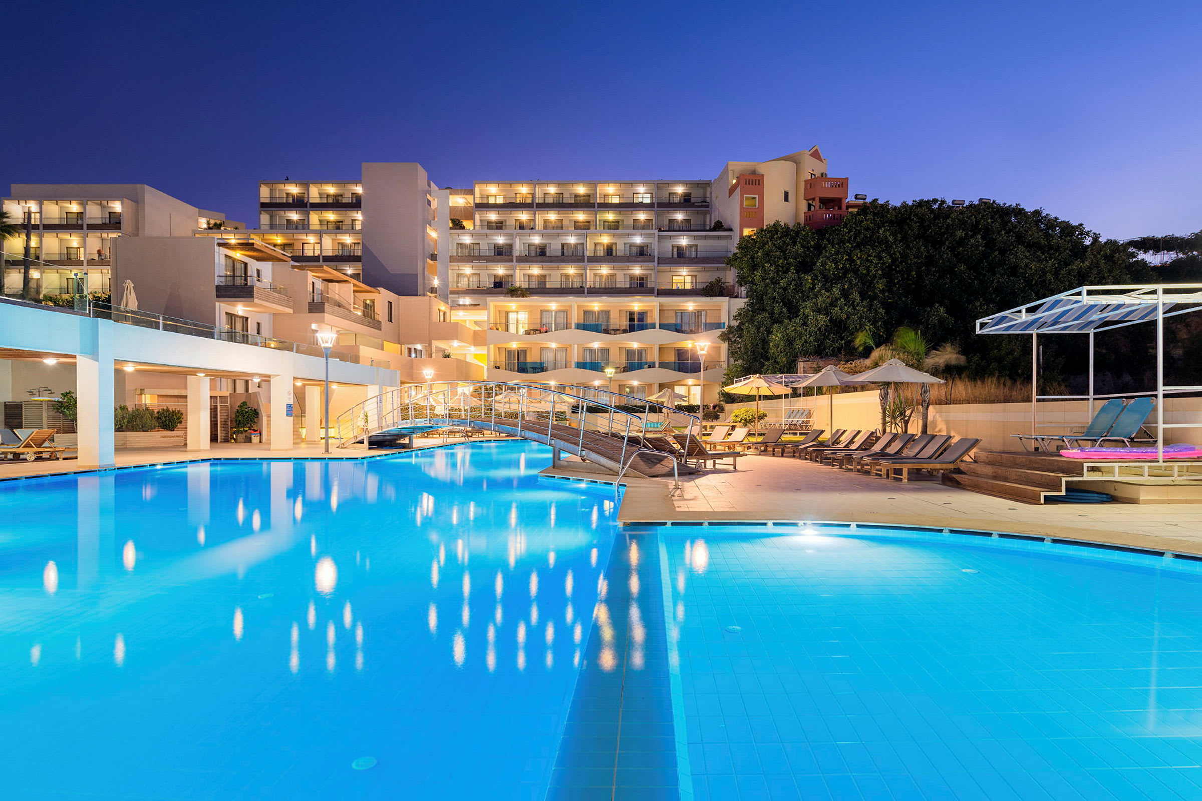 Hotelområde med en oplyst pool og liggestole om aftenen. (AI-genereret tekst)