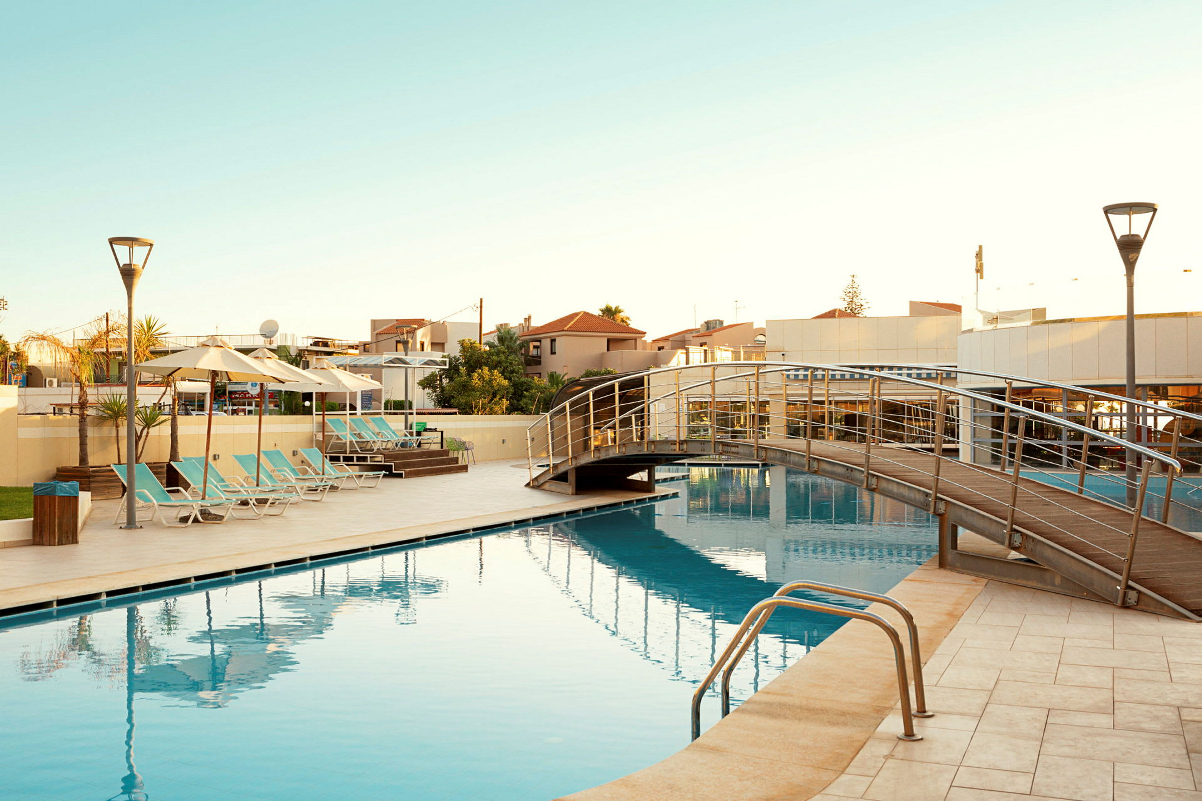 En udendørs swimmingpool med solsenge og en gangbro over vandet. (AI-genereret tekst)