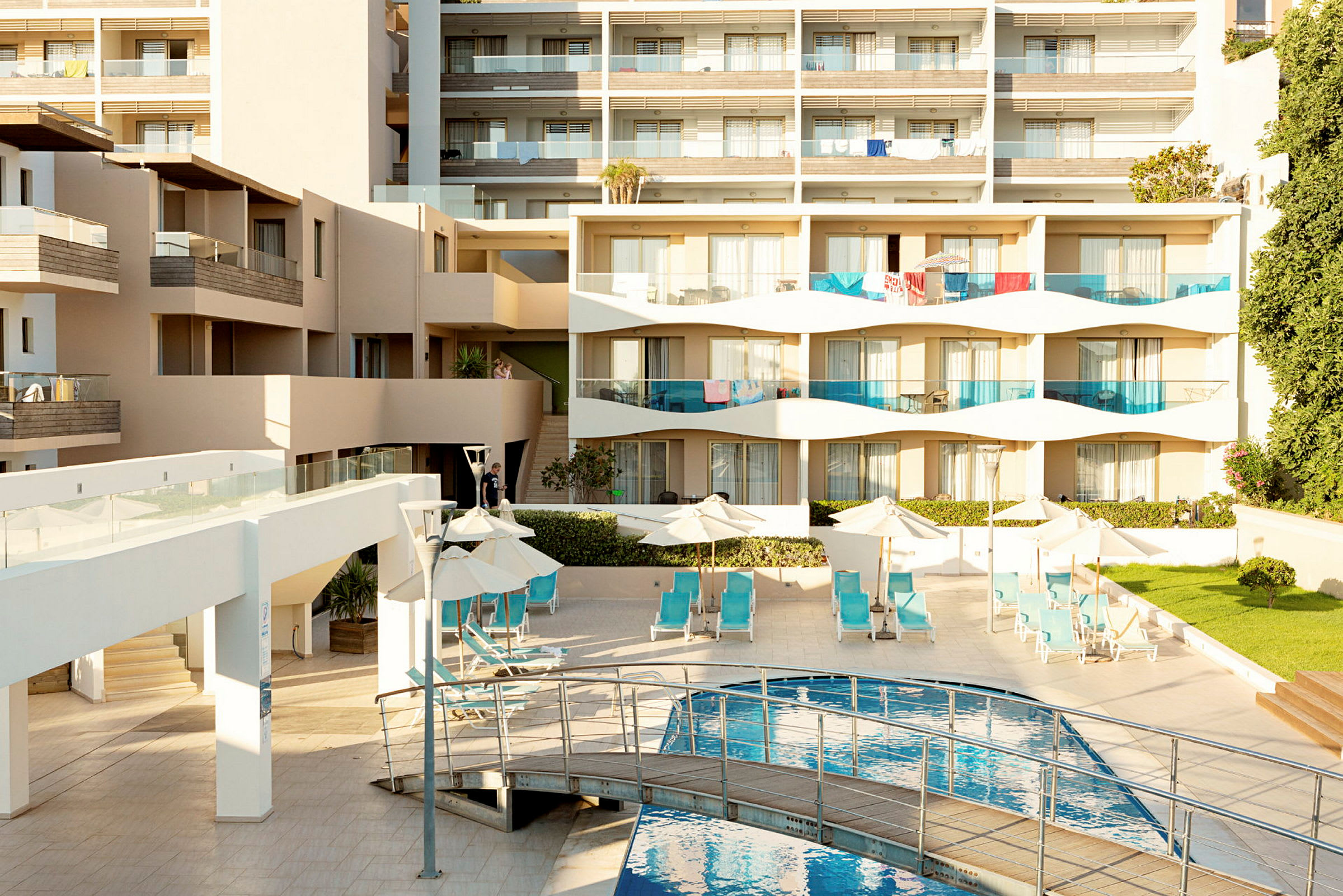 En moderne hotelbygning med altaner, liggestole ved en pool og grønne områder. (AI-genereret tekst)