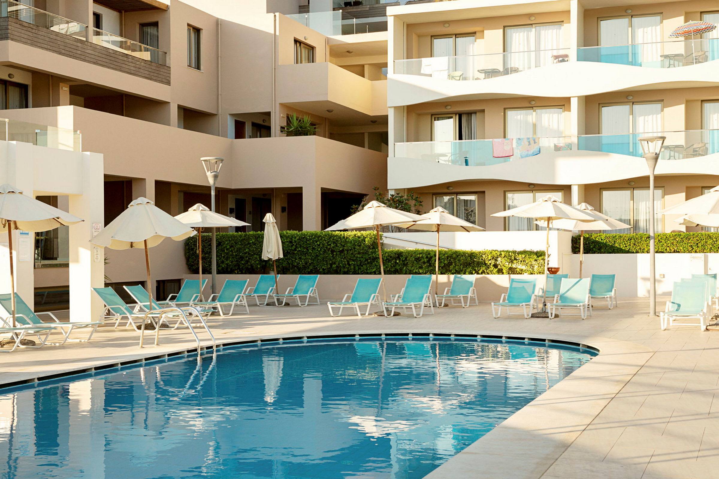 Udendørs pool omgivet af liggestole og parasoller ved siden af en moderne bygning. (AI-genereret tekst)