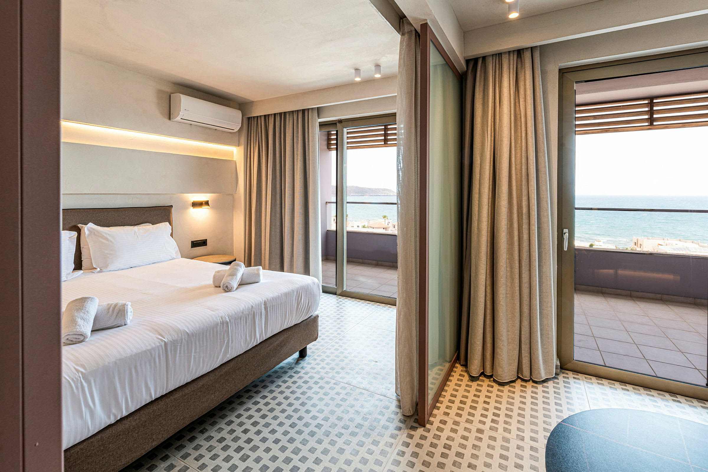 Hotelværelse med seng og håndklæder, store glasdøre der fører ud til en balkon med havudsigt. (AI-genereret tekst)