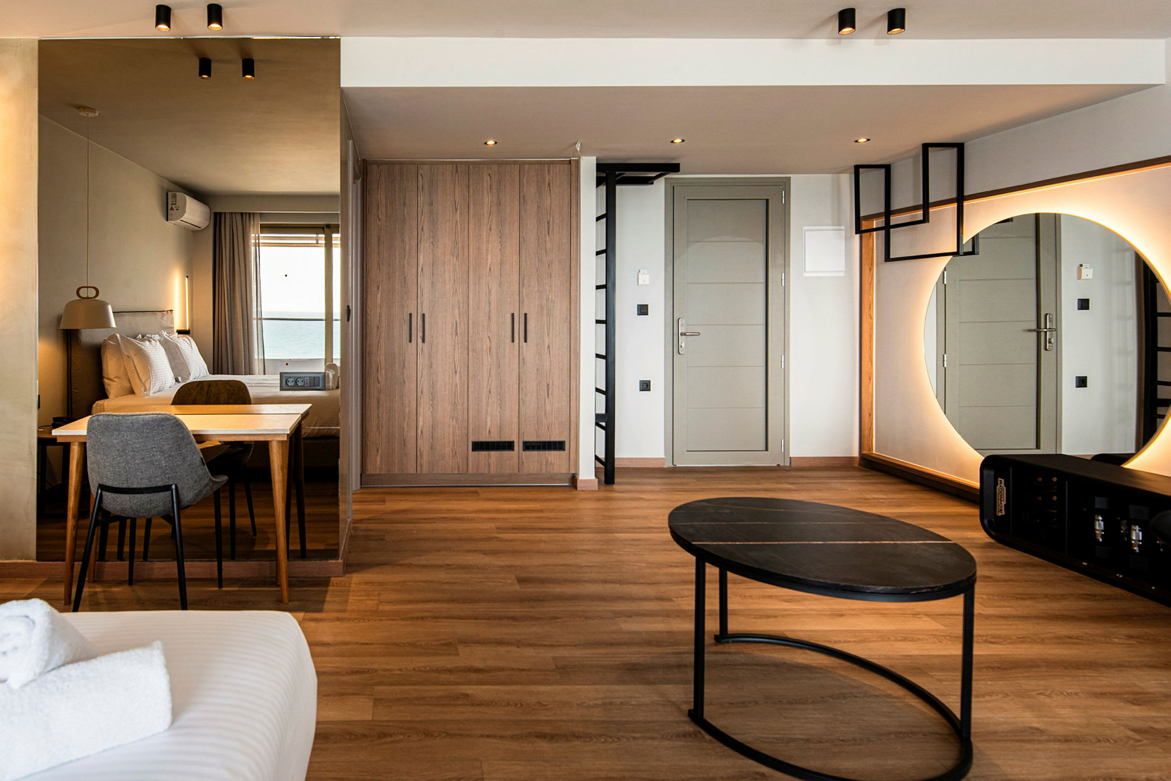 Hotelværelse med moderne indretning, inklusive seng, bord, stol, spejl og garderobe. (AI-genereret tekst)